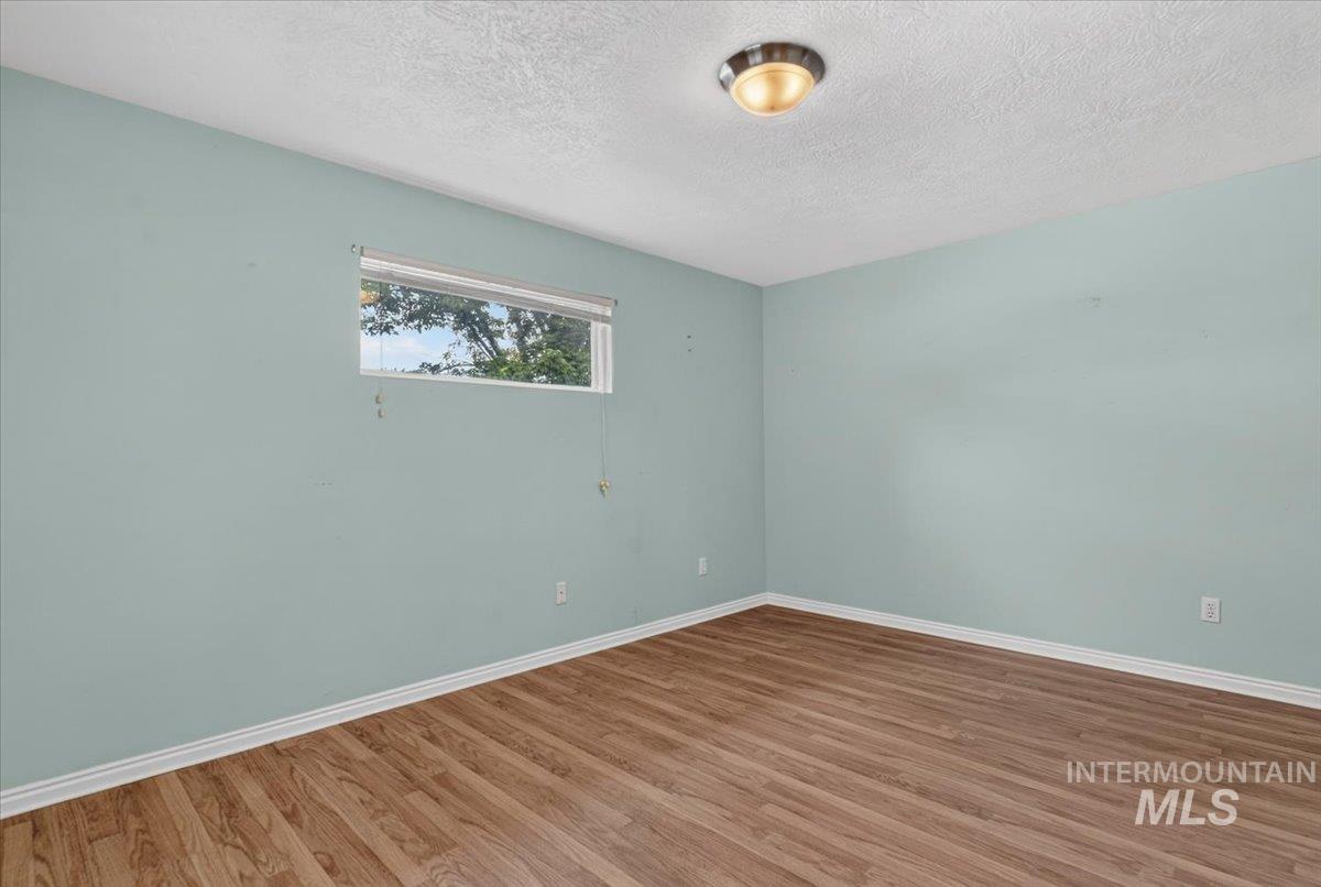 Room featuring wood-finish flooring, a rectangular window with horizontal blinds, and a flush-mount ceiling light fixture