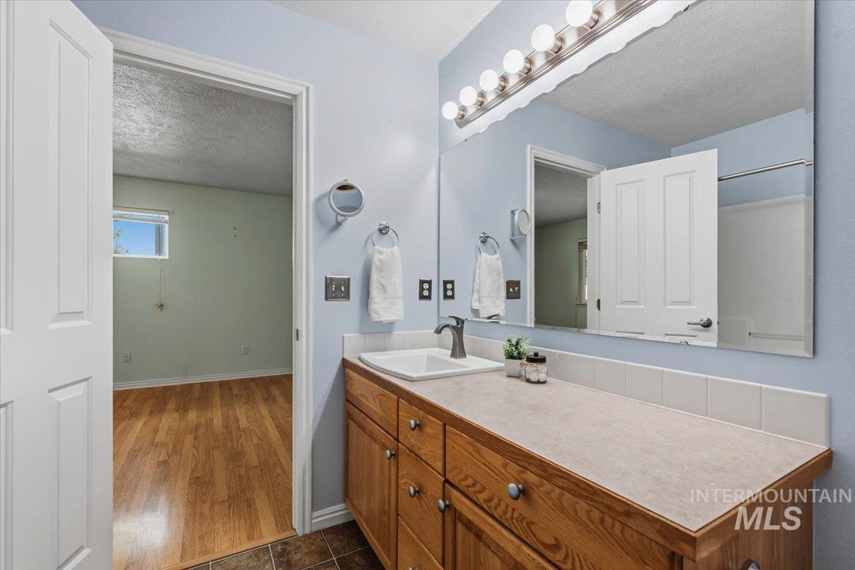 Bathroom vanity featuring a single sink, wood-finish cabinetry, and a large mirror with integrated lighting