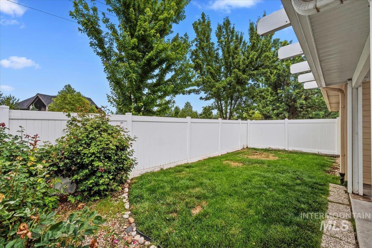 Private backyard featuring a white vinyl fence, established perimeter landscaping, and a manicured lawn
