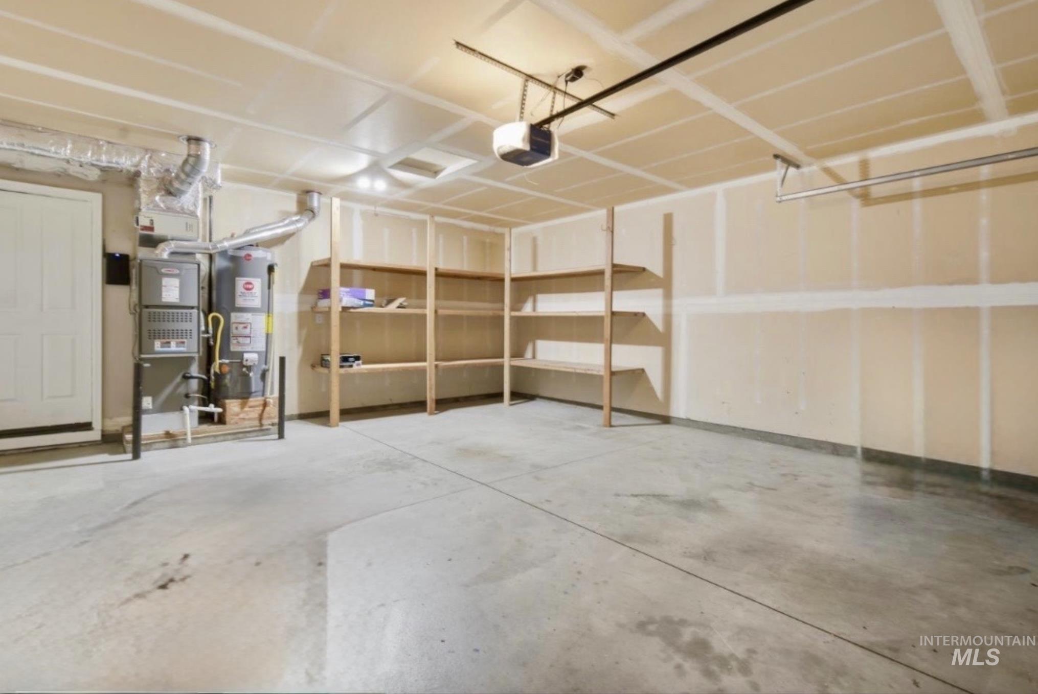 Spacious garage featuring concrete flooring, built-in shelving, an overhead garage door opener, and visible utility systems