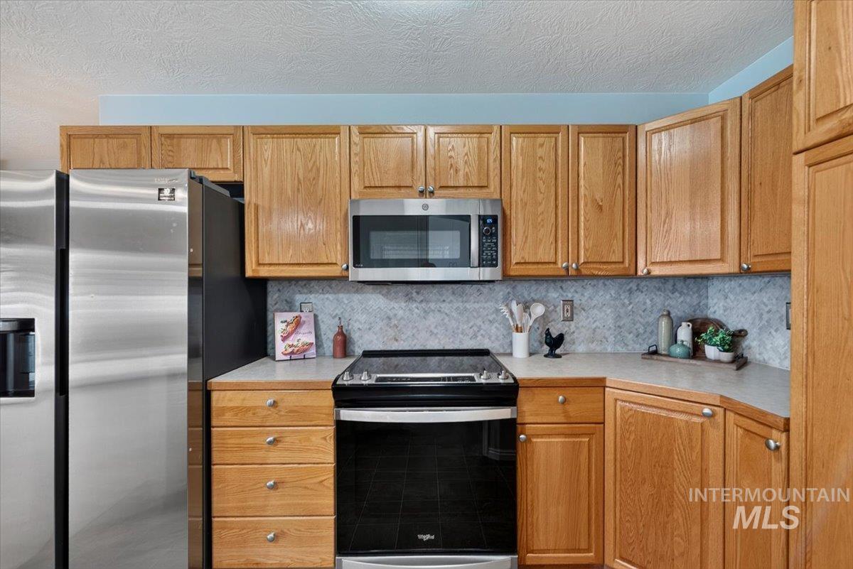 Kitchen featuring oak cabinetry, light-toned countertops, a stainless steel refrigerator, a stainless steel microwave, and a black electric range