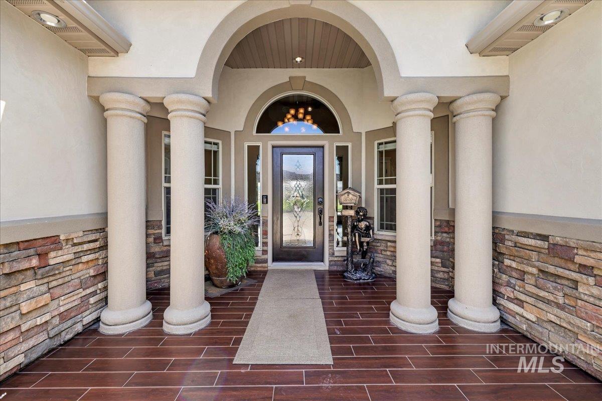View of exterior entry with stone siding, covered porch, and stucco siding