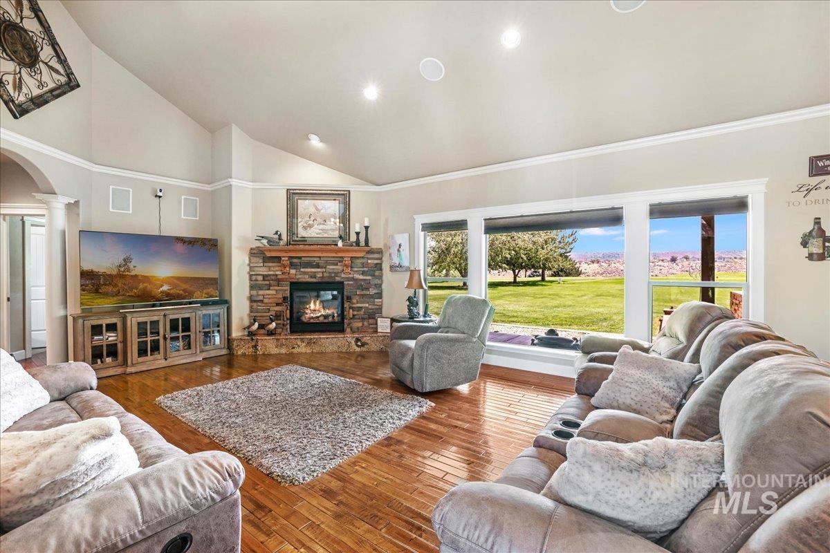 Living room featuring ornate columns, high vaulted ceiling, a stone fireplace, recessed lighting, and wood finished floors