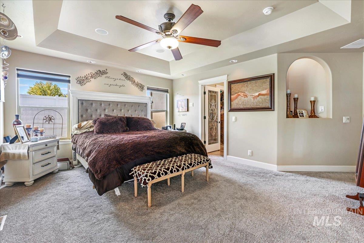 Bedroom with a raised ceiling, light carpet, and ceiling fan