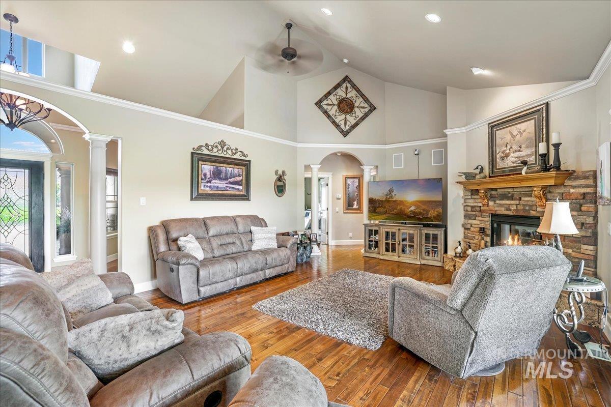 Living area with ornate columns, arched walkways, a ceiling fan, hardwood / wood-style floors, and high vaulted ceiling