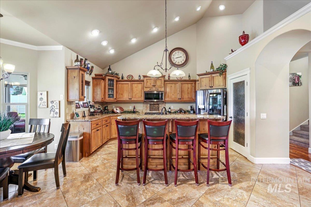 Kitchen with brown cabinetry, arched walkways, a kitchen island, glass insert cabinets, and appliances with stainless steel finishes