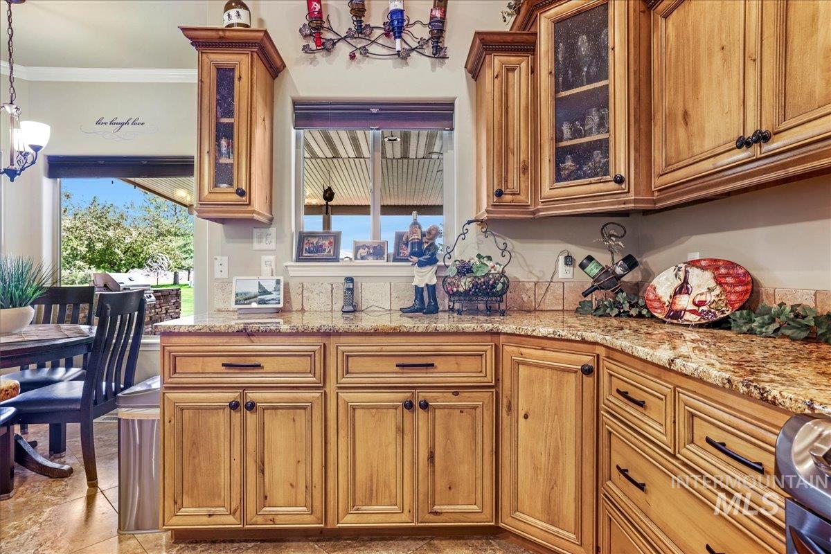 Kitchen featuring a chandelier, light stone counters, brown cabinets, and ornamental molding