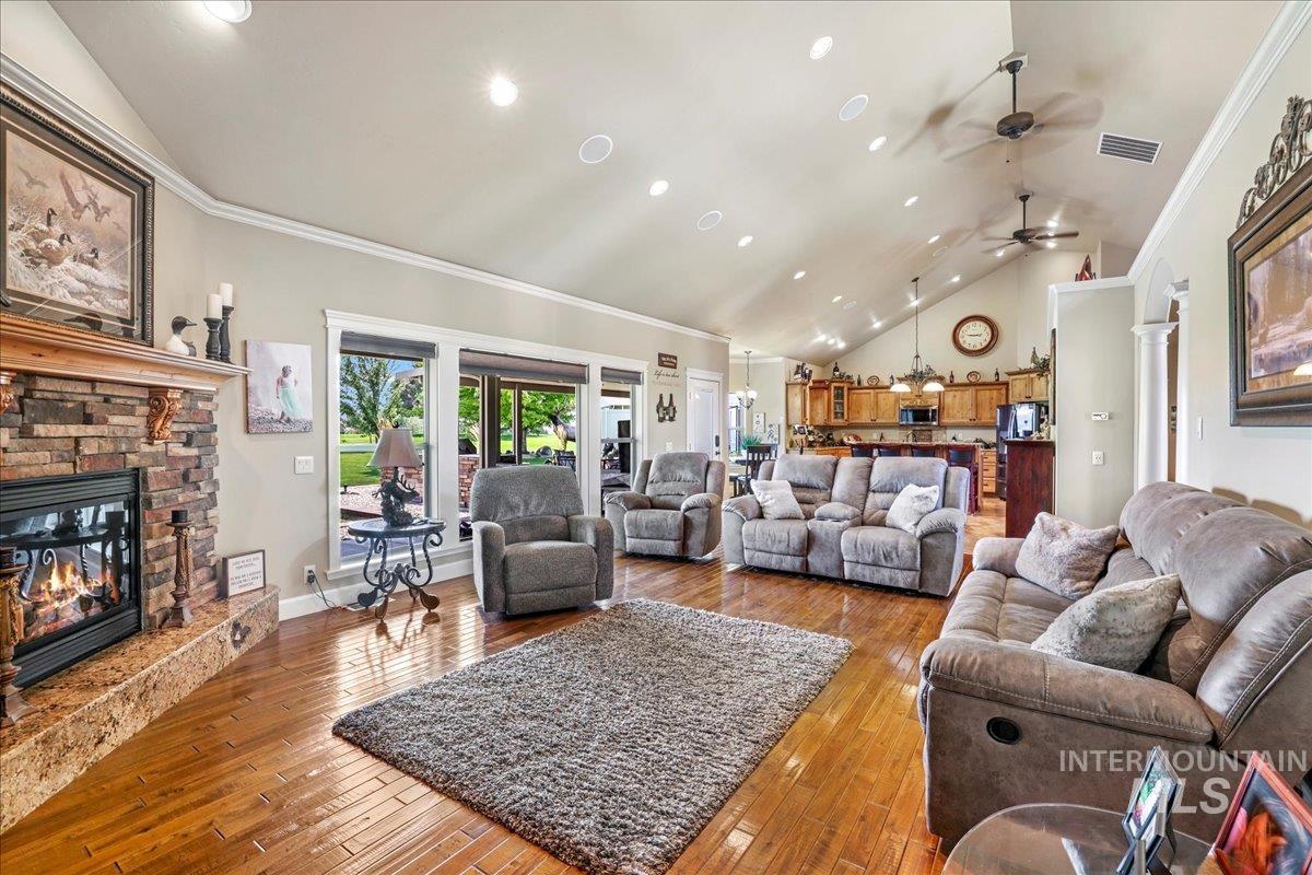 Living area featuring vaulted ceiling, a ceiling fan, a fireplace, ornamental molding, and hardwood / wood-style flooring