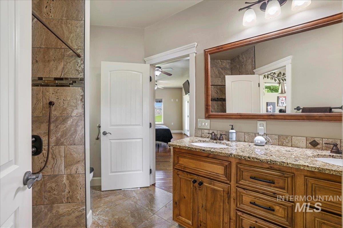 Bathroom with double vanity, a ceiling fan, healthy amount of natural light, and a tile shower