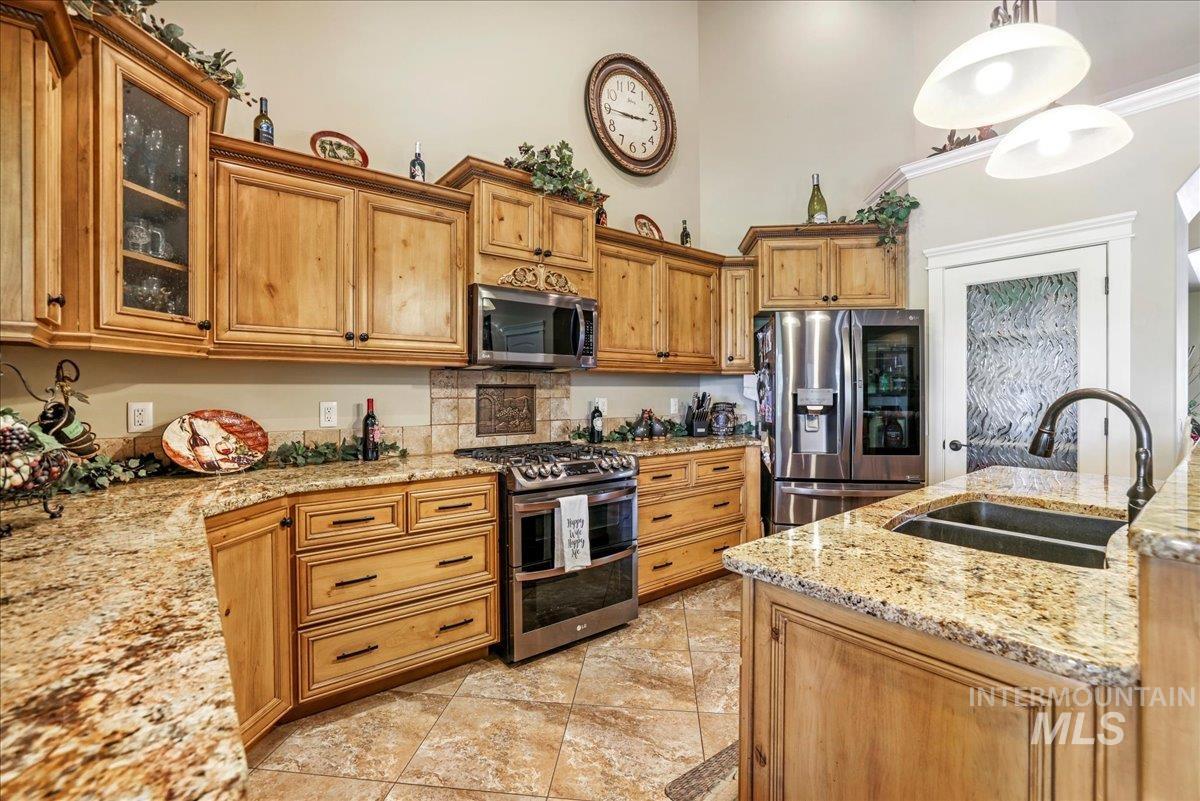 Kitchen with stainless steel appliances, a towering ceiling, light stone countertops, glass insert cabinets, and pendant lighting