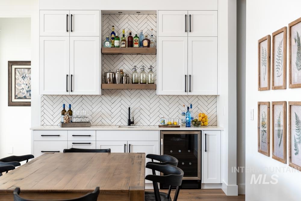 Bar area with wine cooler, white cabinetry, open shelves, light stone countertops, and backsplash