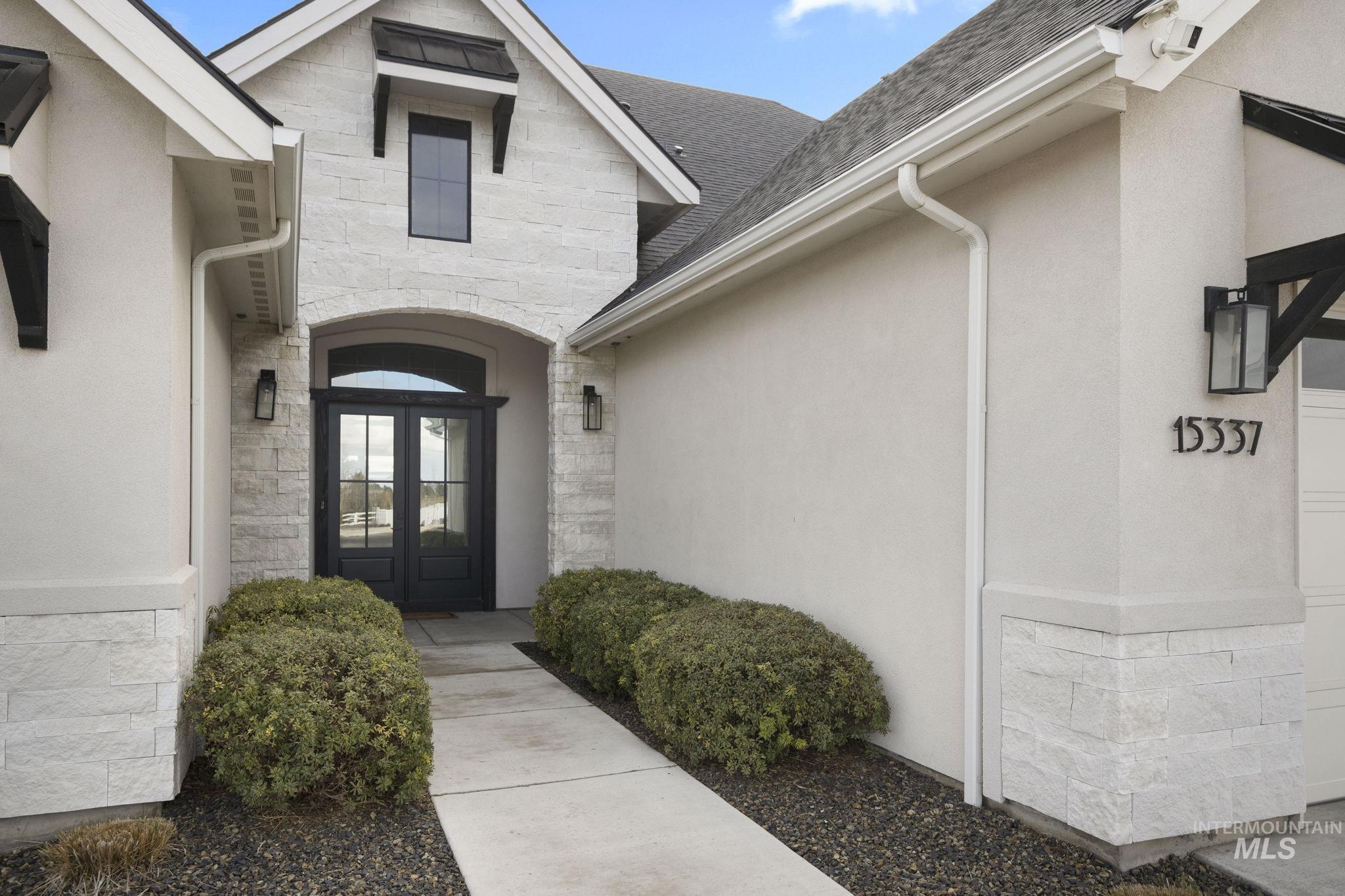 Property entrance with stone siding, a shingled roof, stucco siding, and french doors