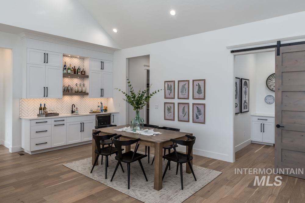 Dining space featuring a barn door, vaulted ceiling, wet bar, light wood-style flooring, and recessed lighting