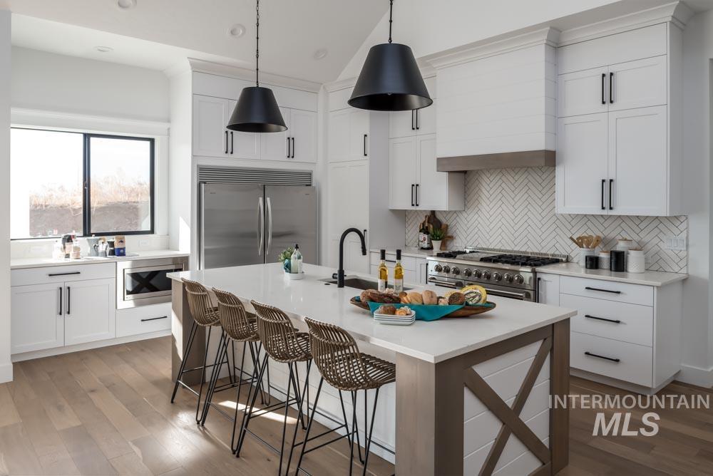 Kitchen with built in appliances, light wood-style flooring, a breakfast bar, white cabinets, and lofted ceiling