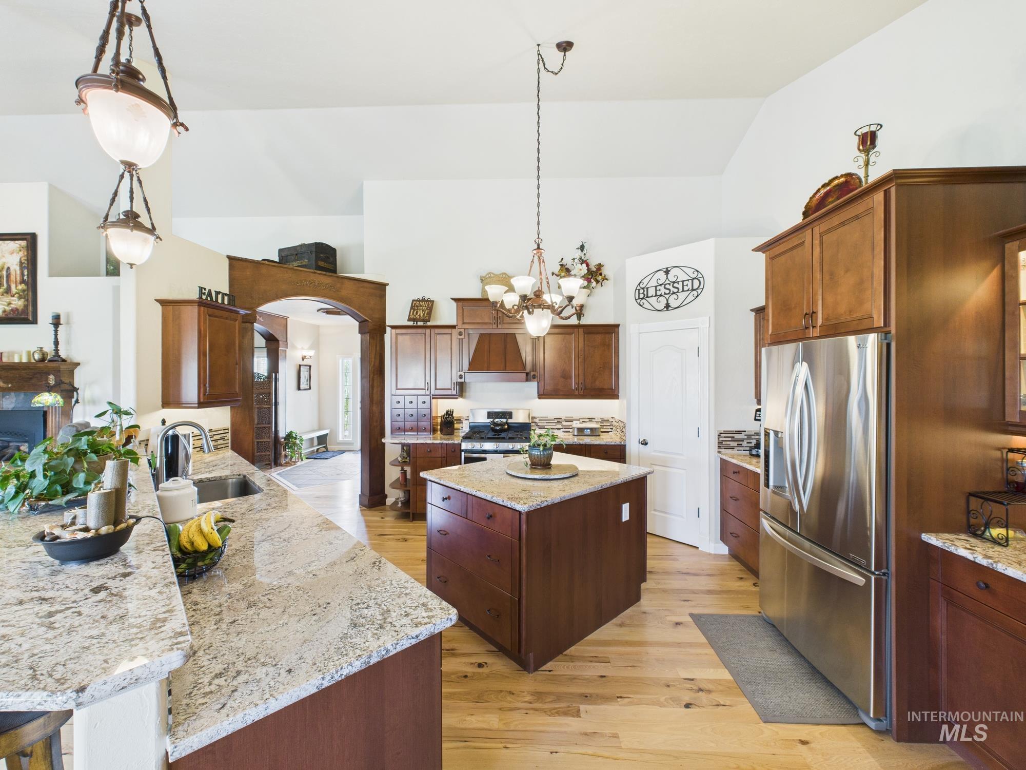 Kitchen with light wood finished floors, appliances with stainless steel finishes, hanging light fixtures, granite countertops, and high vaulted ceiling