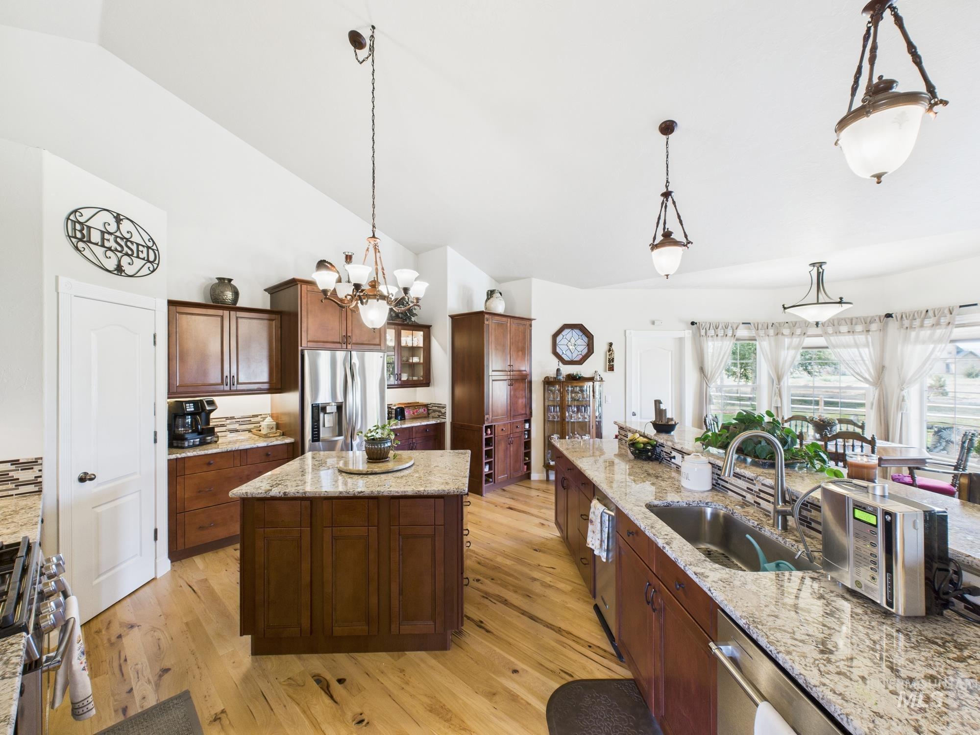 Kitchen with decorative light fixtures, granite countertops, stainless steel appliances, light wood-style floors, and high vaulted ceiling