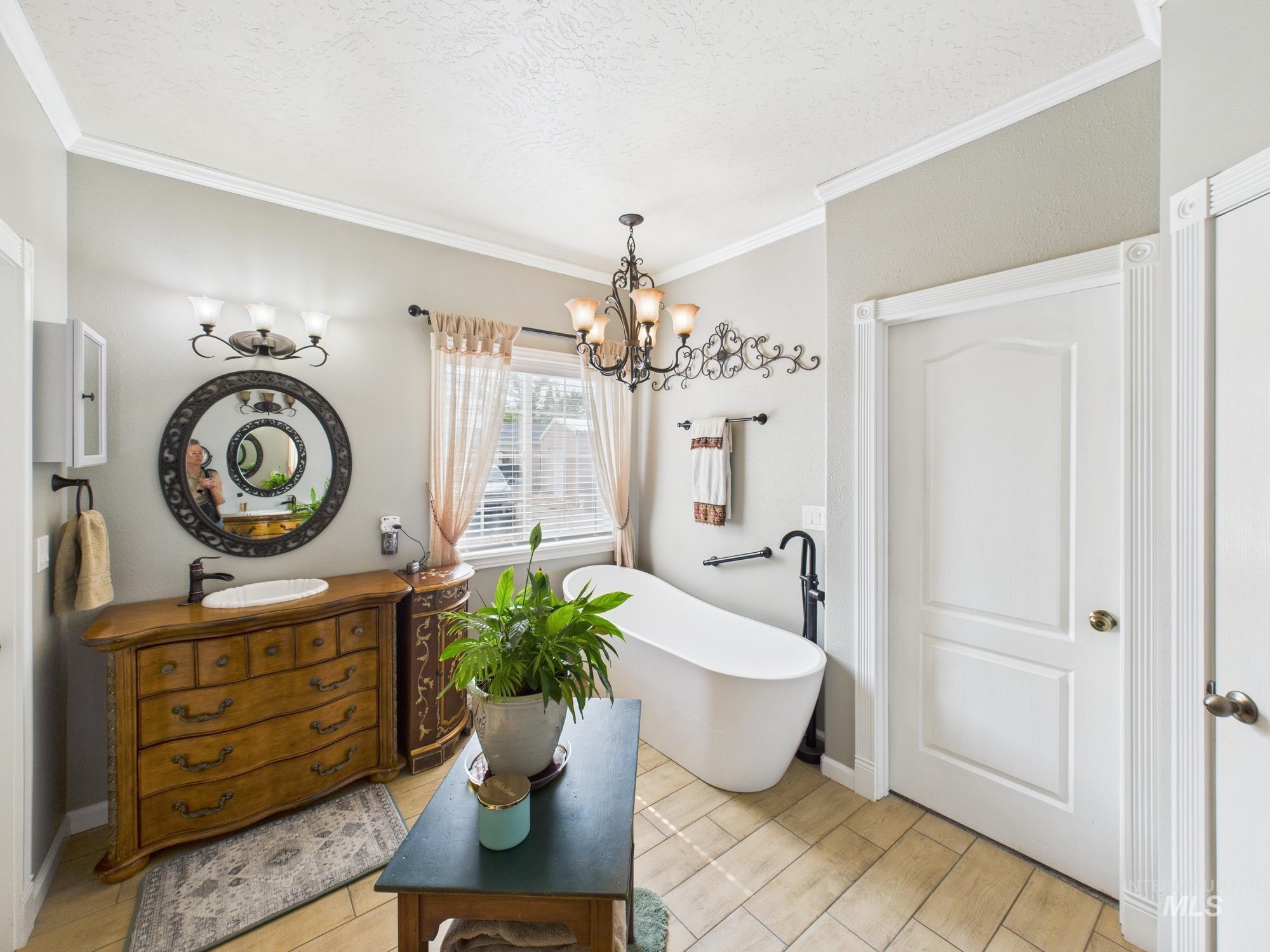 Full bathroom featuring vanity, a freestanding tub, wood tiled floors, crown molding, and a chandelier