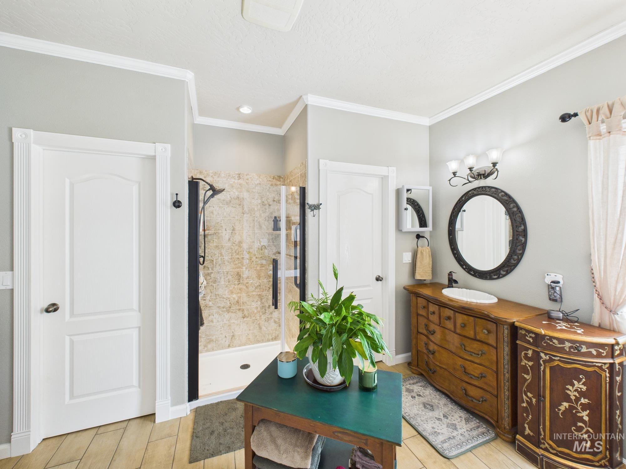 Bathroom with vanity, a shower stall, crown molding, and light wood-type flooring