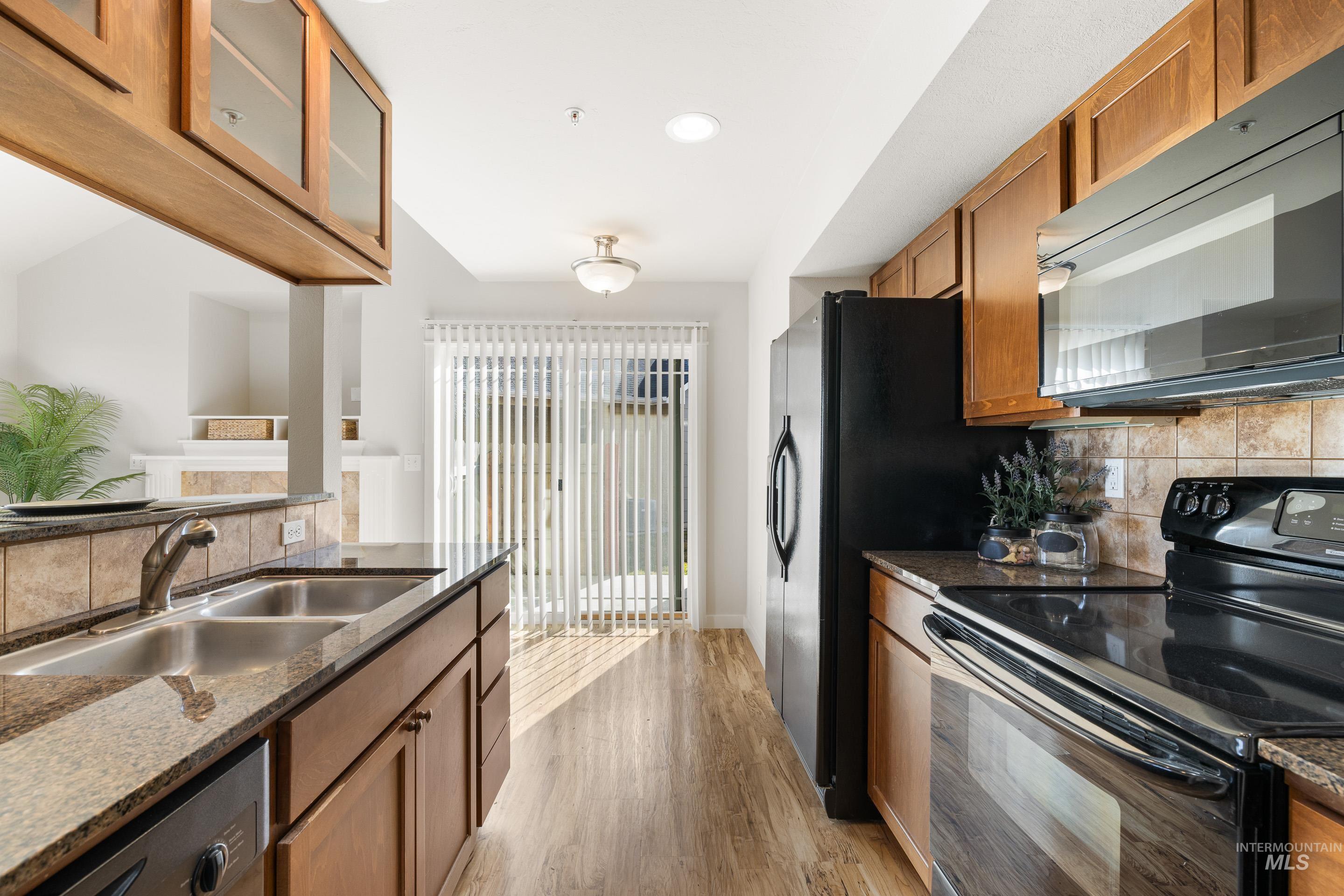 Kitchen with black appliances, backsplash, wood finish cabinets, light wood finished floors, and dark stone counters