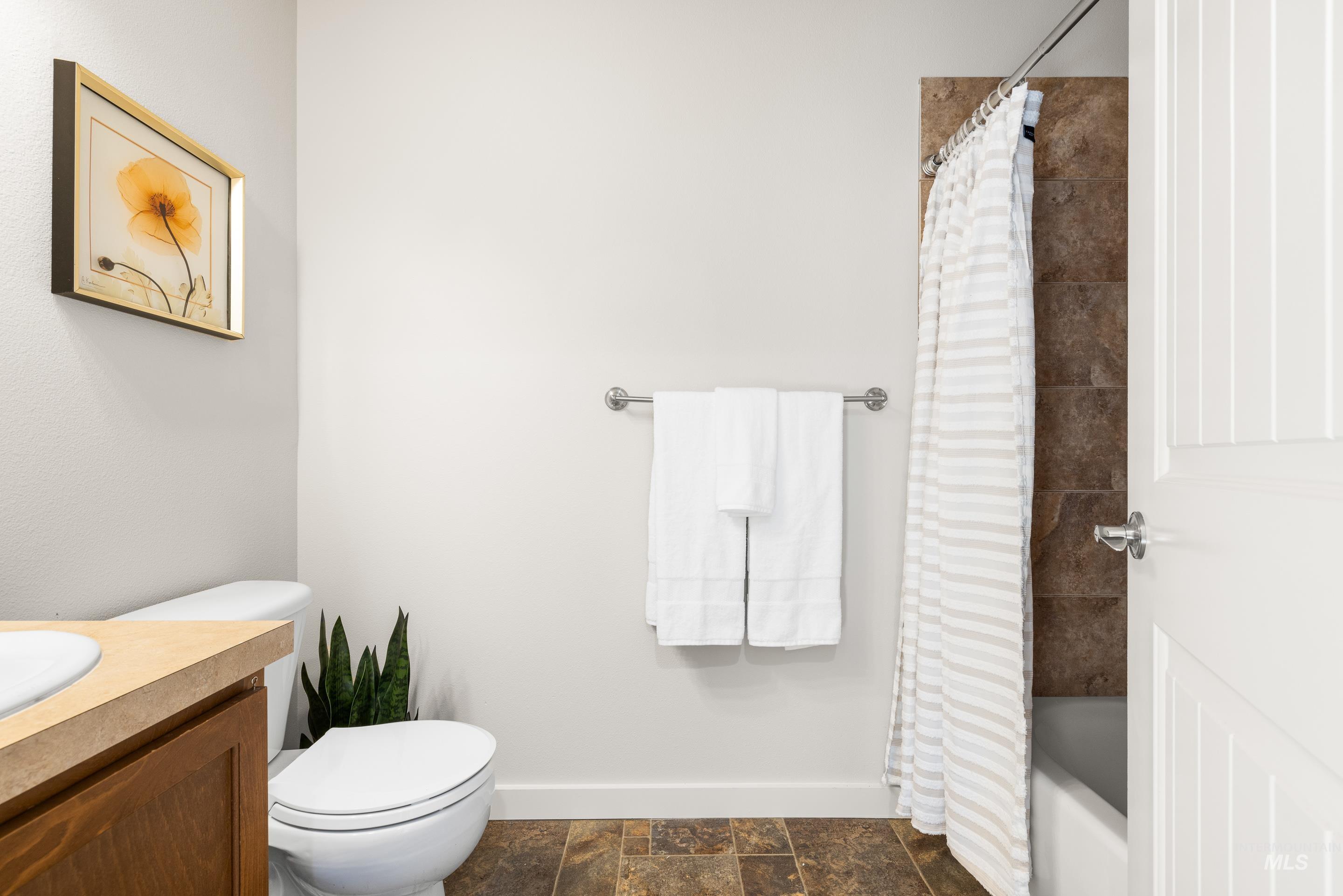 Bathroom featuring vanity, shower / bath combo, and dark stone finish flooring