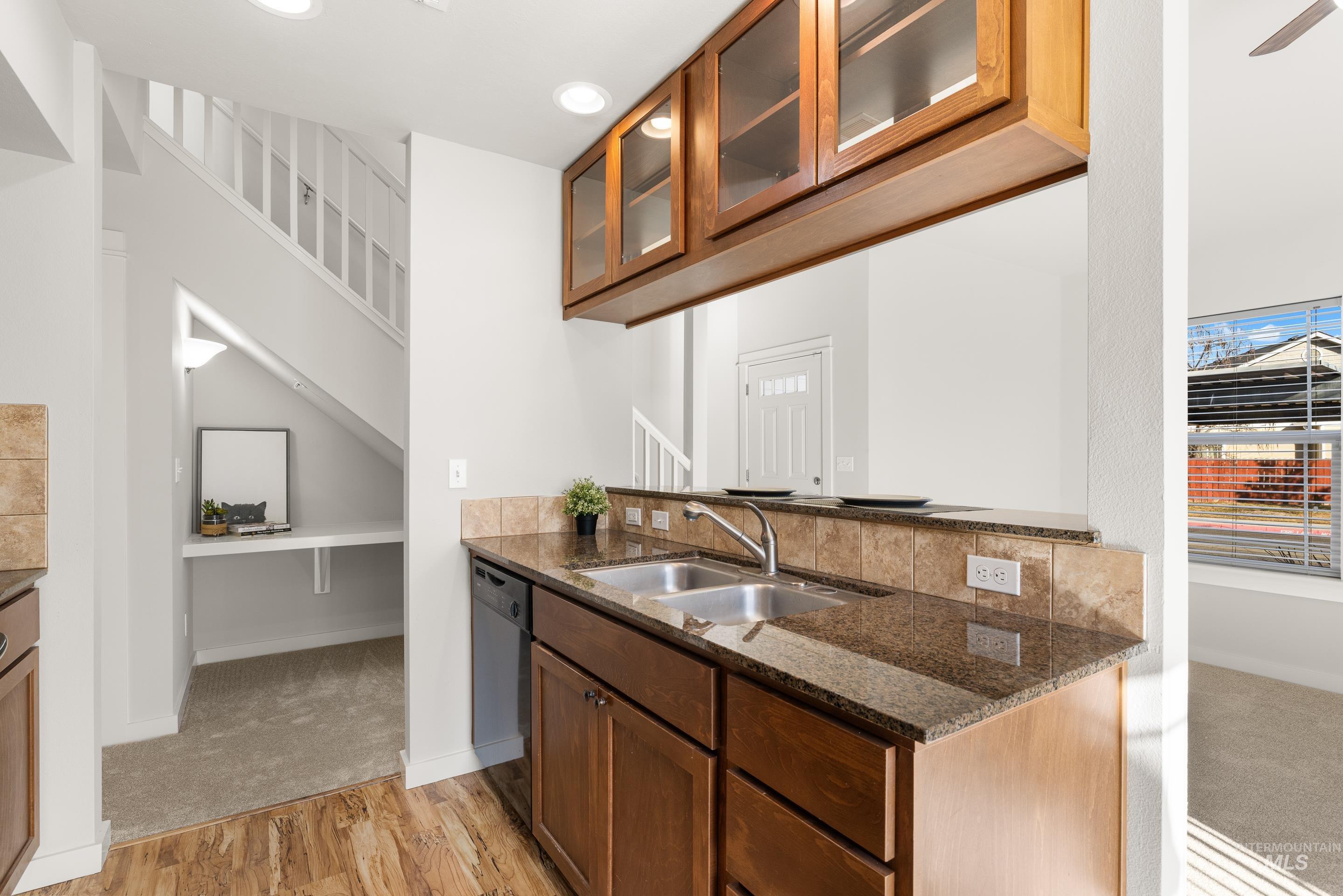 Kitchen featuring glass insert cabinets, dark stone countertops, light wood finished floors, black dishwasher, and wood finish cabinetry