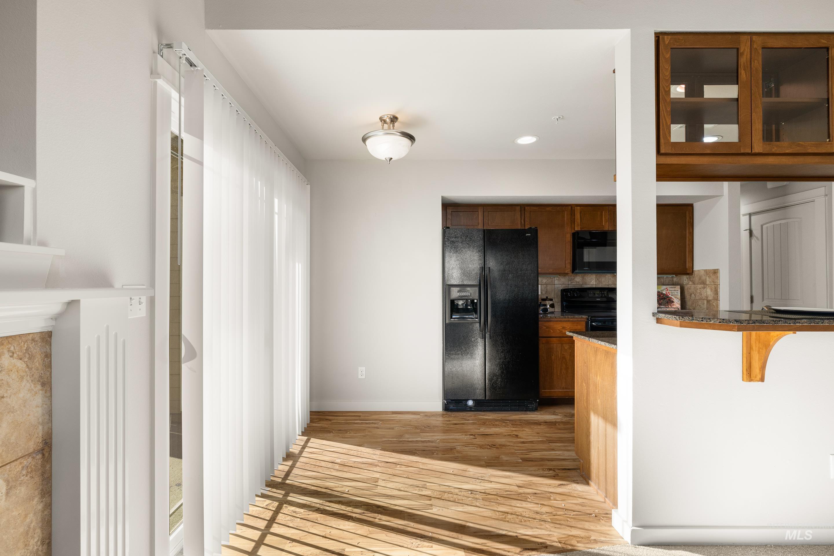 Kitchen with wood finish cabinetry, black appliances, light wood-type flooring, glass fronted cabinets, and backsplash