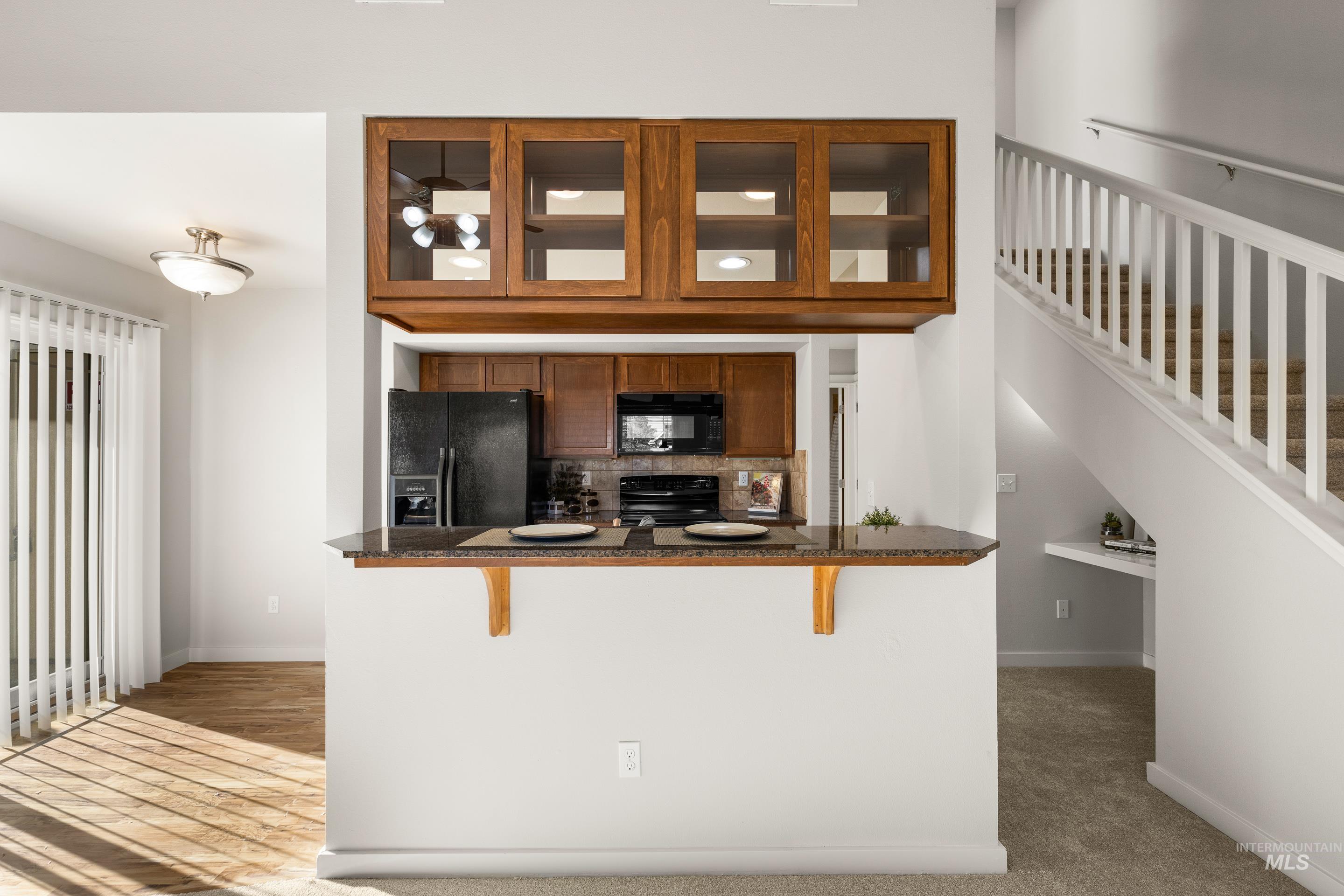Kitchen with wood finish cabinetry, a kitchen bar, black appliances, decorative backsplash, and dark stone counters