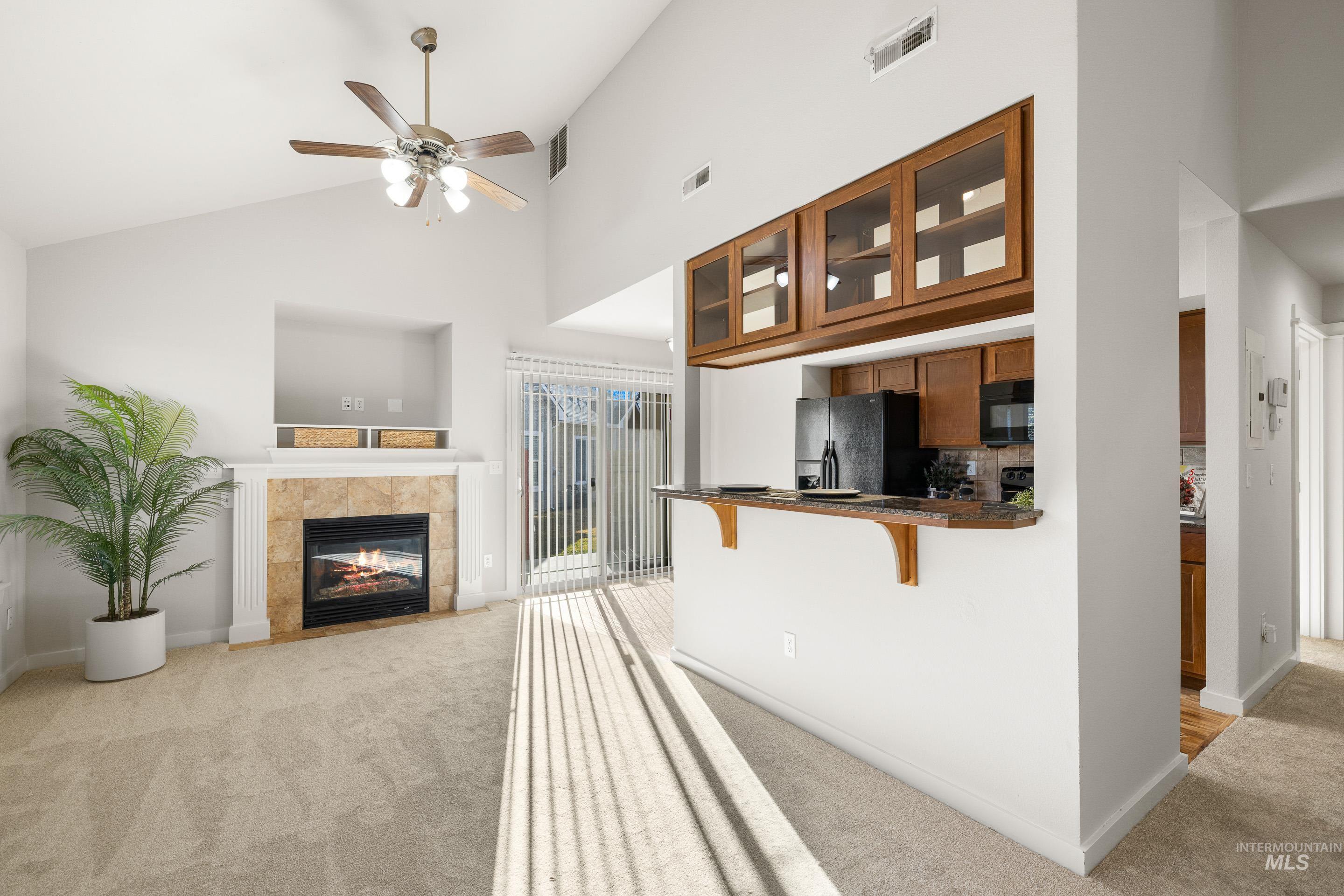 Living area featuring light colored carpet, a tile fireplace, a ceiling fan, and lofted ceiling
