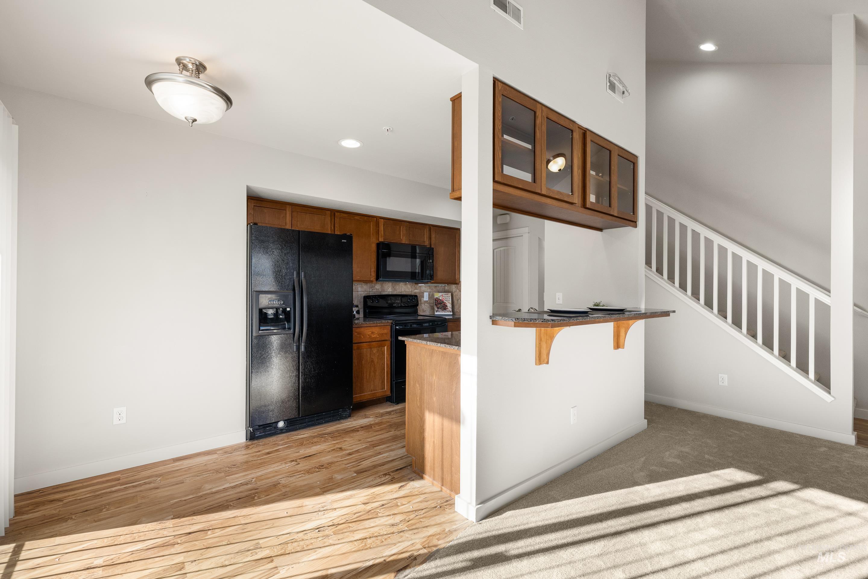 Kitchen featuring a breakfast bar area, wood finish cabinets, black appliances, glass insert cabinets, and light wood finished floors