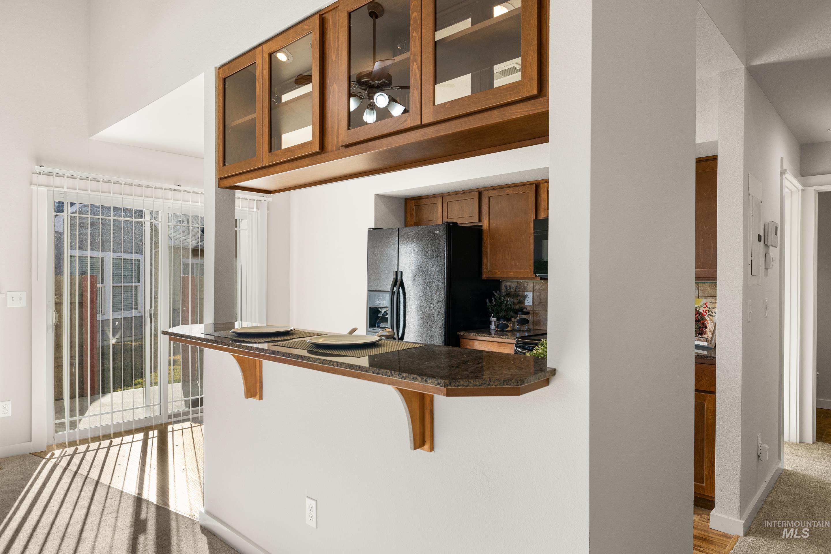 Kitchen featuring a breakfast bar, wood finish cabinetry, light carpet, glass insert cabinets, and black refrigerator with ice dispenser