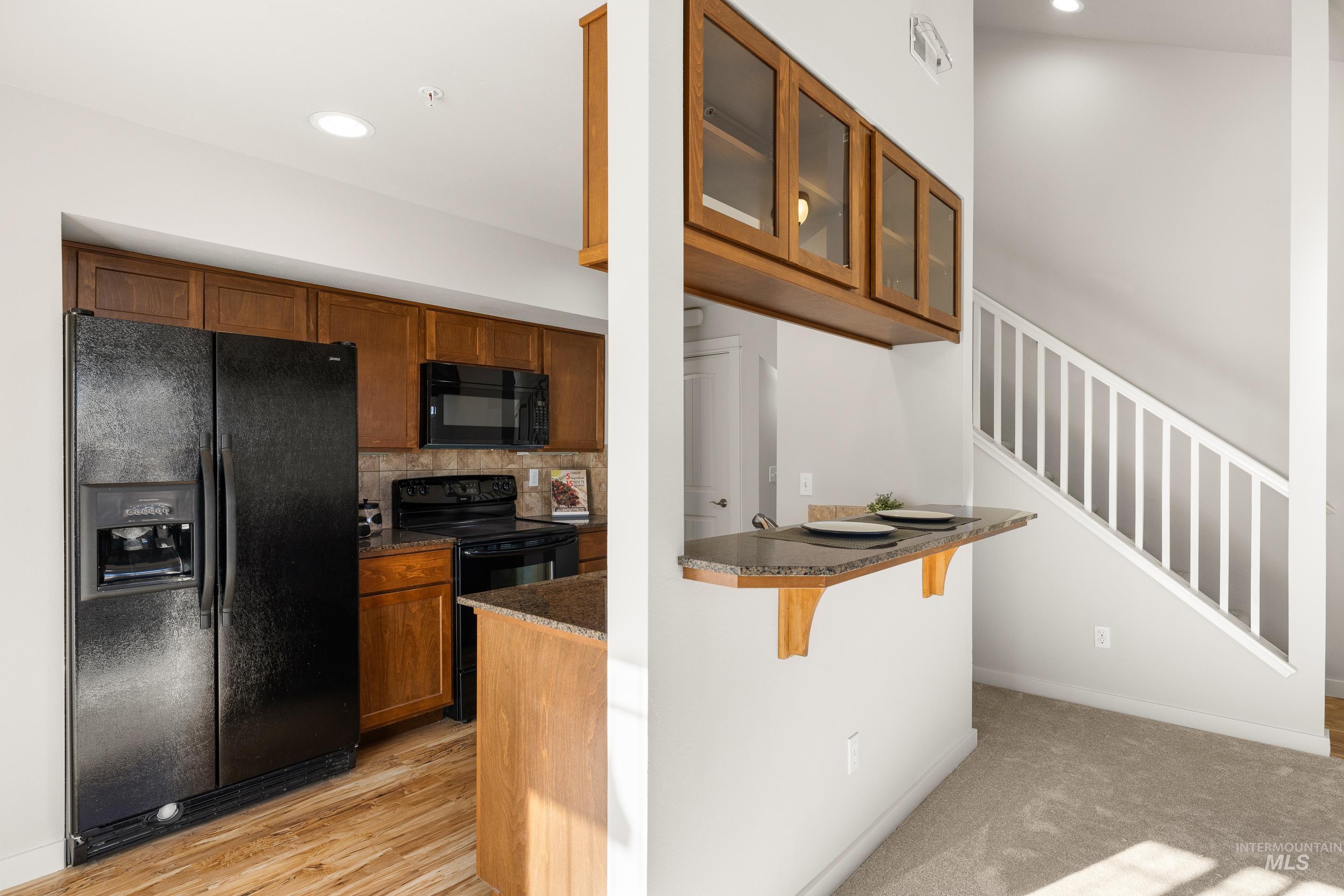 Kitchen featuring a breakfast bar area, black appliances, glass fronted cabinets, wood finish cabinets, and recessed lighting