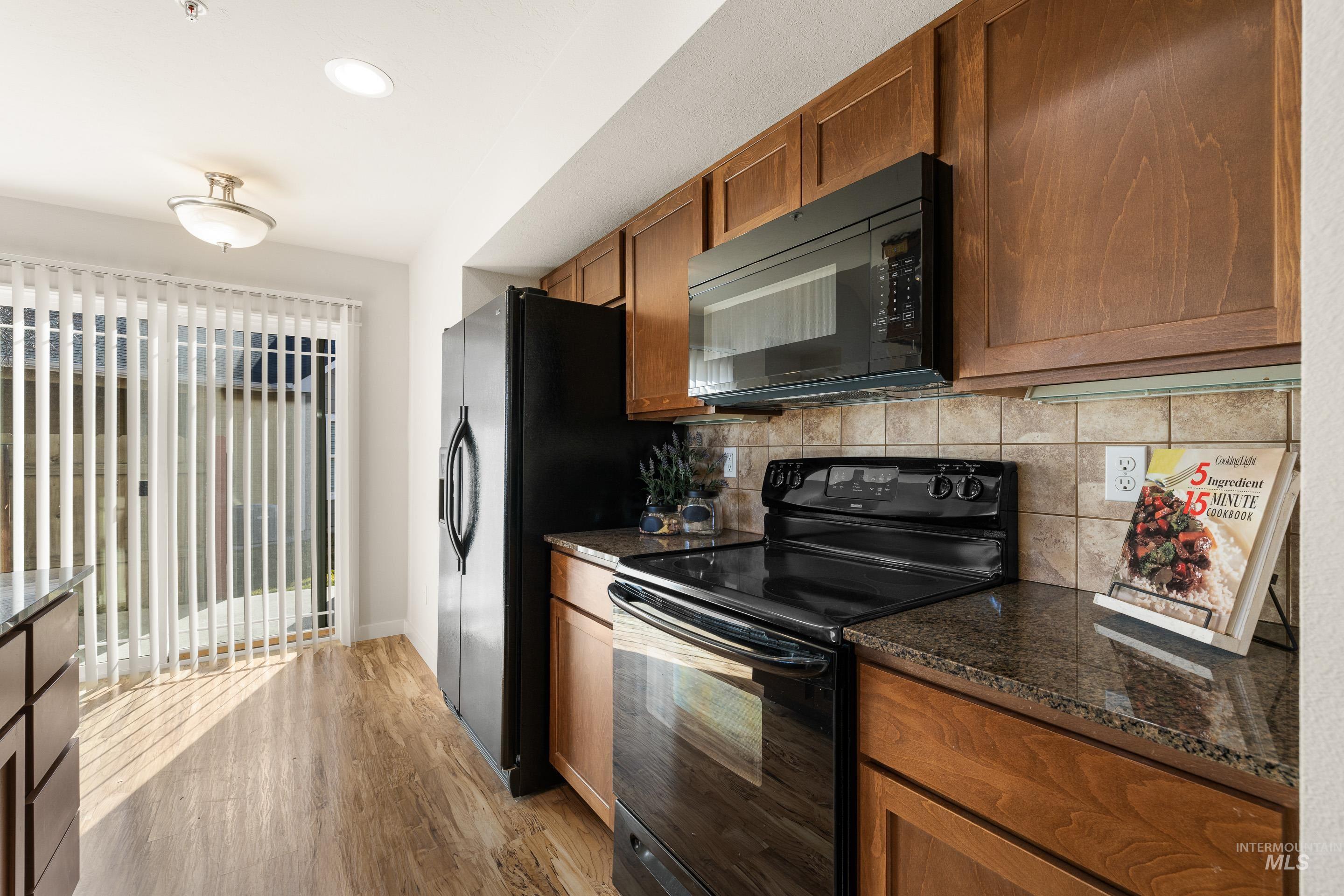 Kitchen with black appliances, wood finish cabinets, dark stone counters, and light wood-type flooring