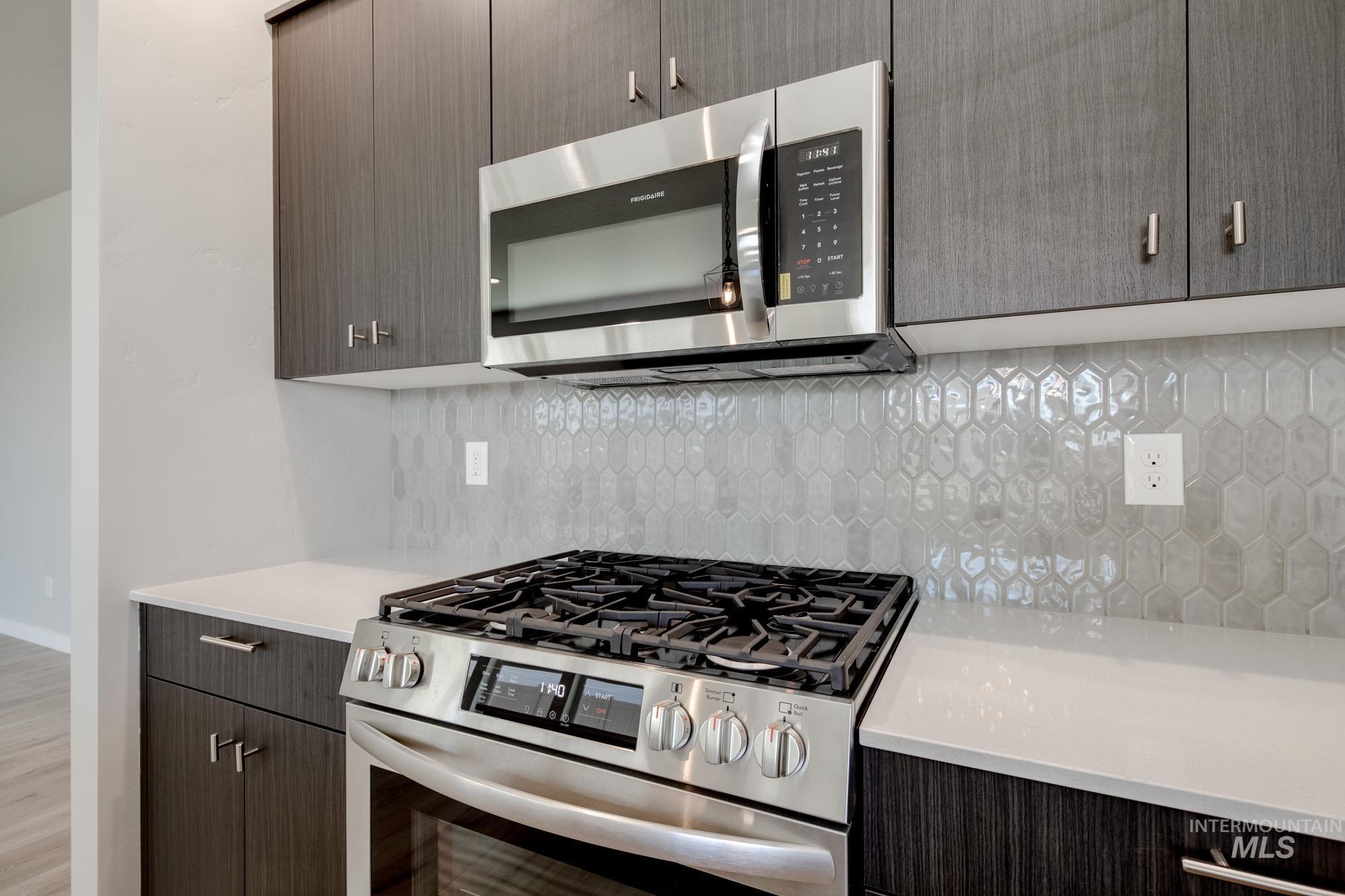 Kitchen featuring appliances with stainless steel finishes, light countertops, backsplash, and wood finished floors
