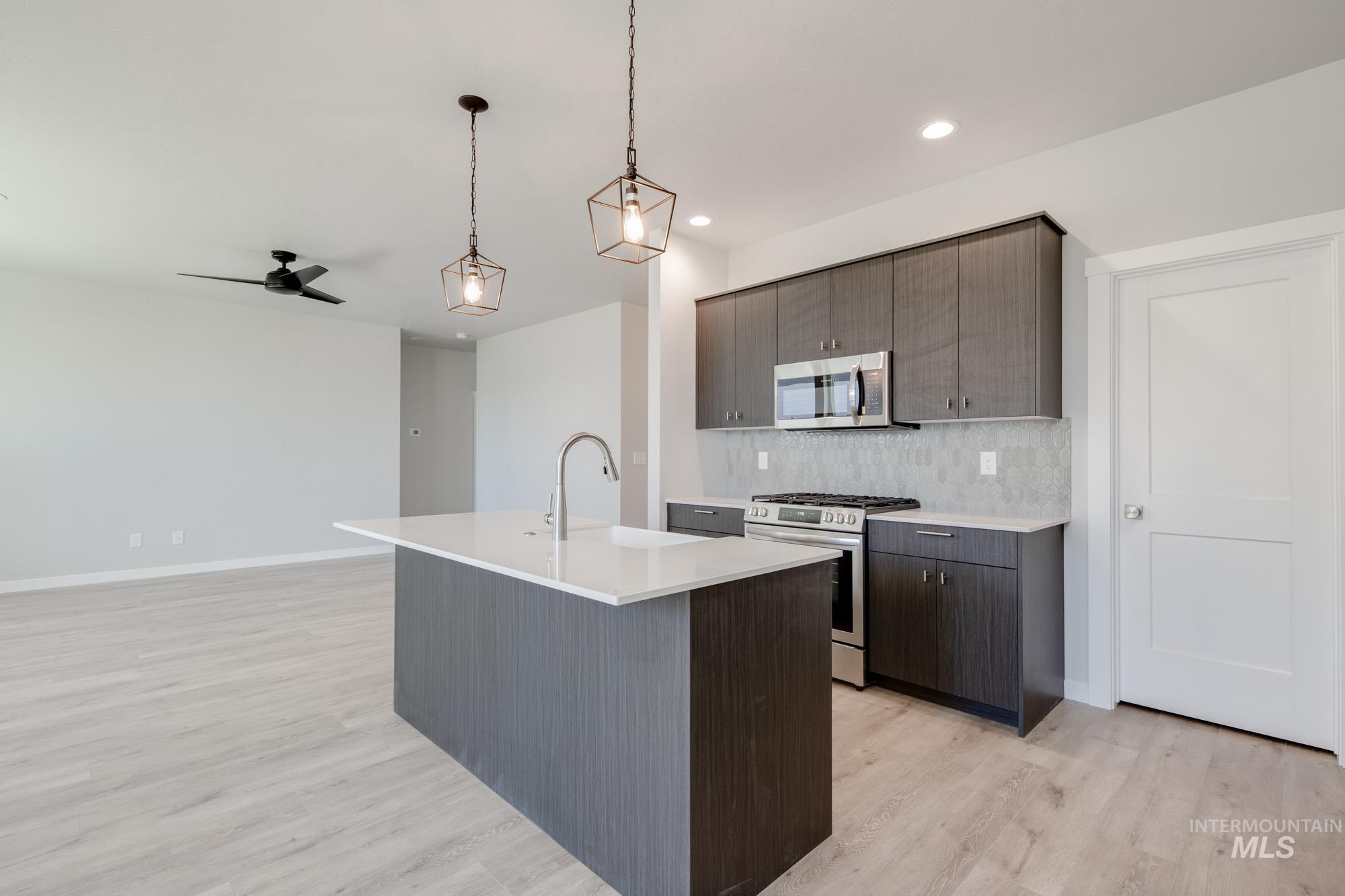 Kitchen with appliances with stainless steel finishes, light wood finished floors, backsplash, light countertops, and ceiling fan
