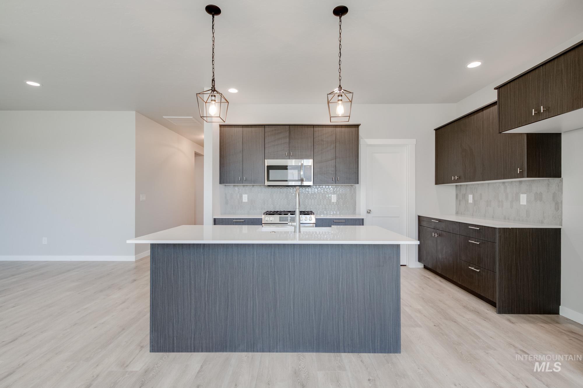 Kitchen with stainless steel appliances, light countertops, tasteful backsplash, light wood-style floors, and dark brown cabinetry