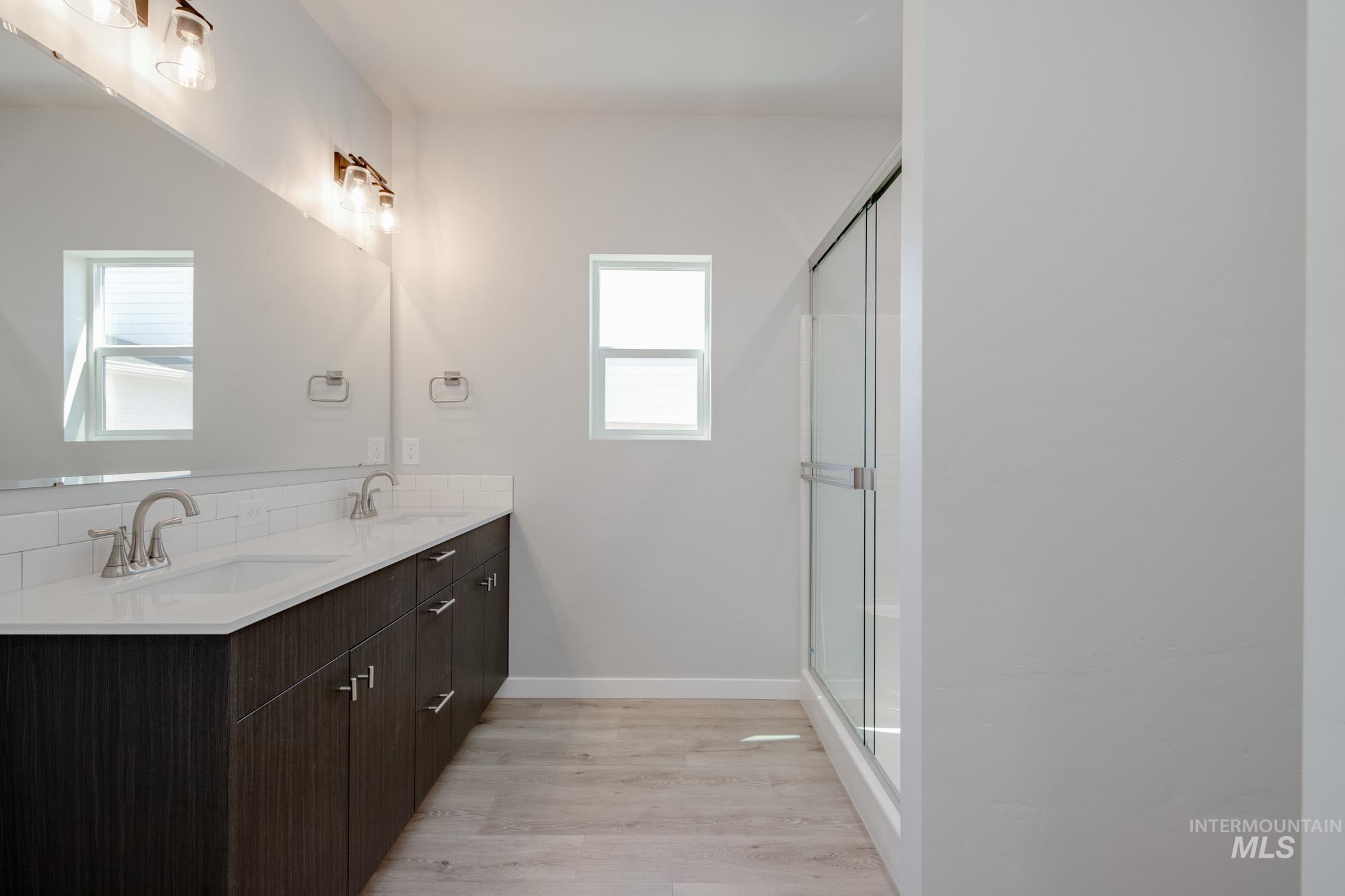 Bathroom with plenty of natural light, double vanity, wood finished floors, and a shower with door