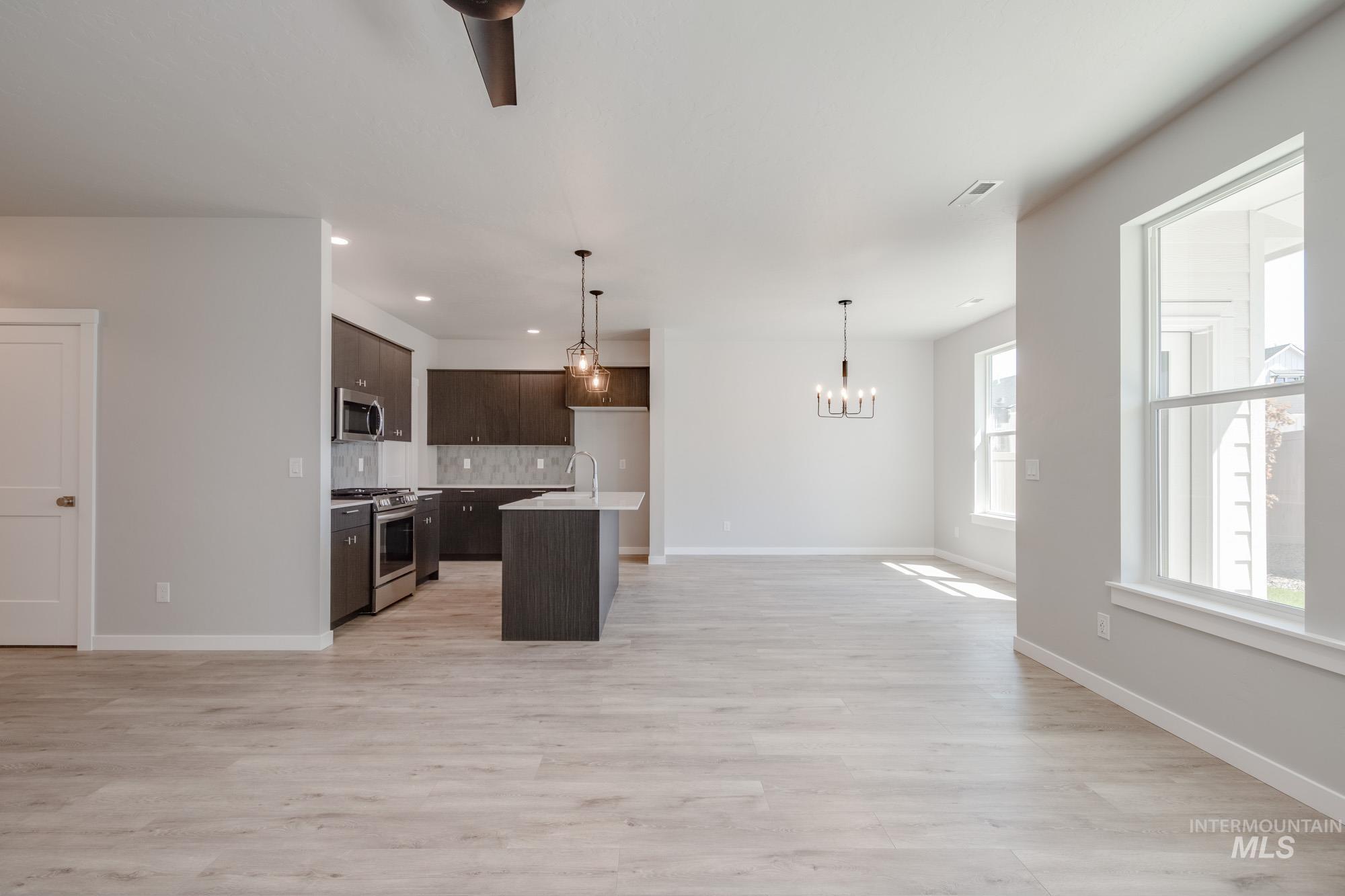 Kitchen with appliances with stainless steel finishes, open floor plan, dark brown cabinets, a chandelier, and backsplash