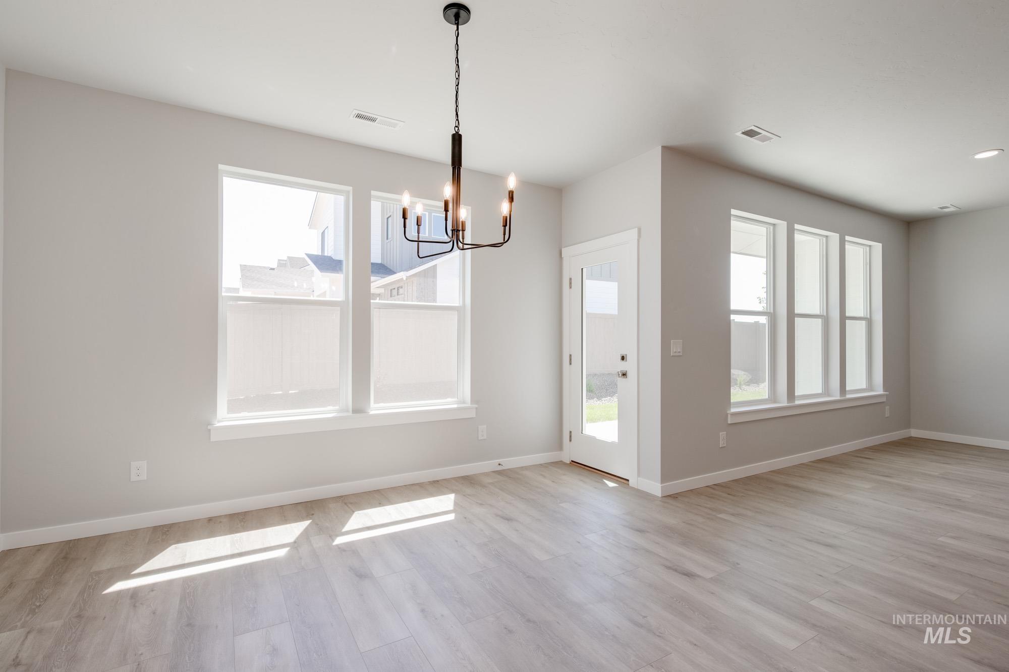 Unfurnished dining area featuring a chandelier, healthy amount of natural light, and light wood finished floors