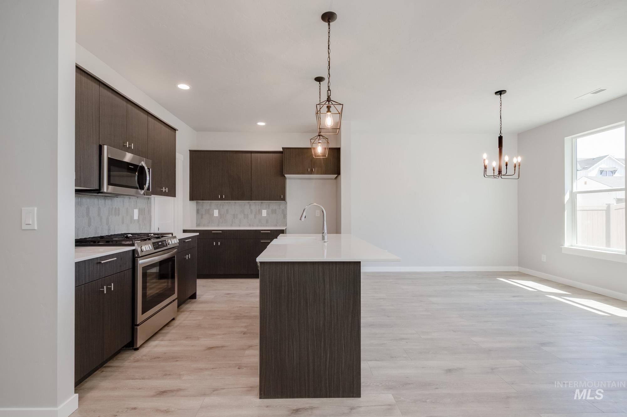 Kitchen with stainless steel appliances, light countertops, decorative backsplash, dark brown cabinets, and light wood-style floors