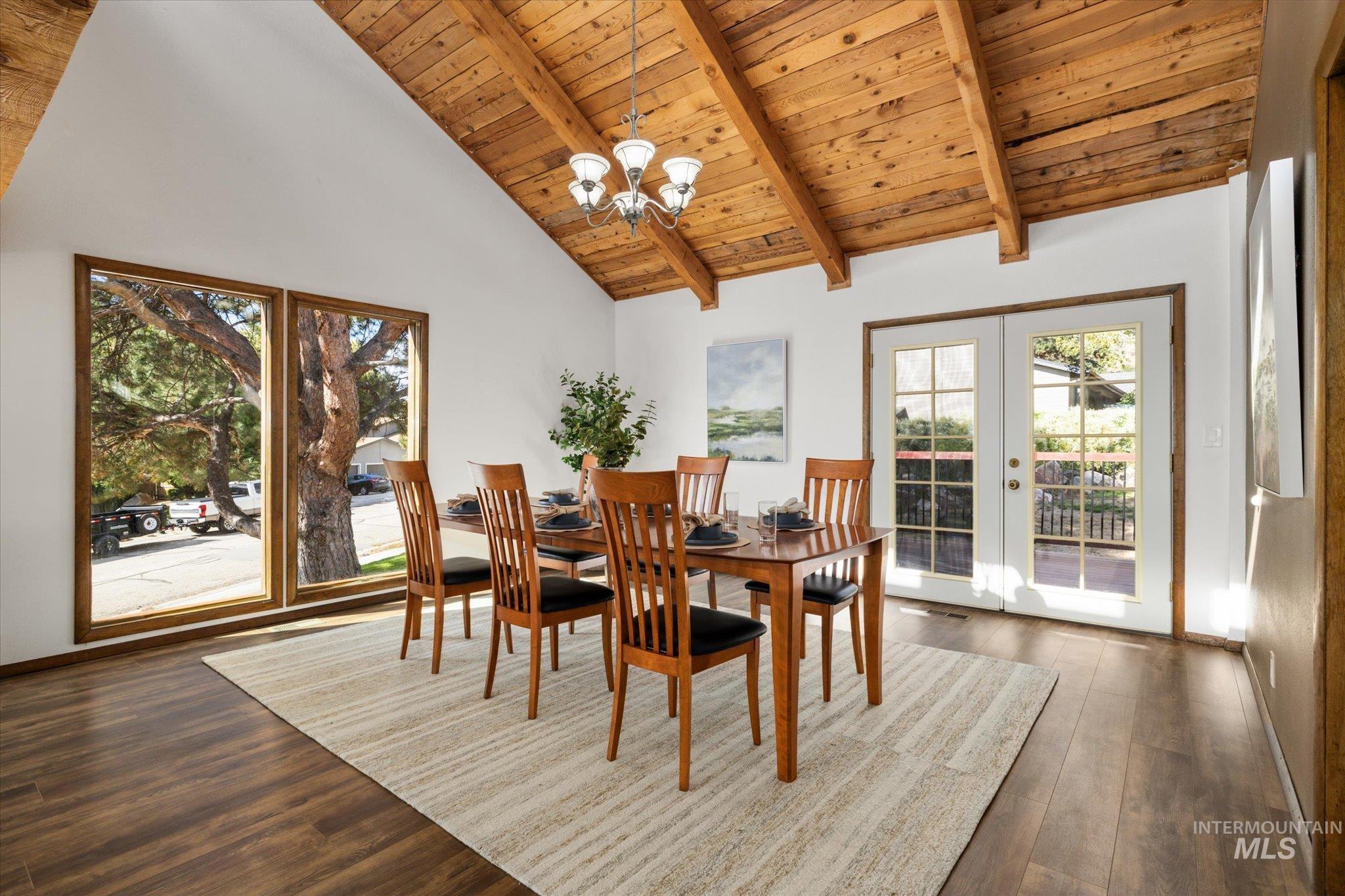 Dining area with a wooden ceiling with exposed beams, high vaulted ceiling, a chandelier, dark wood-type flooring, and french doors