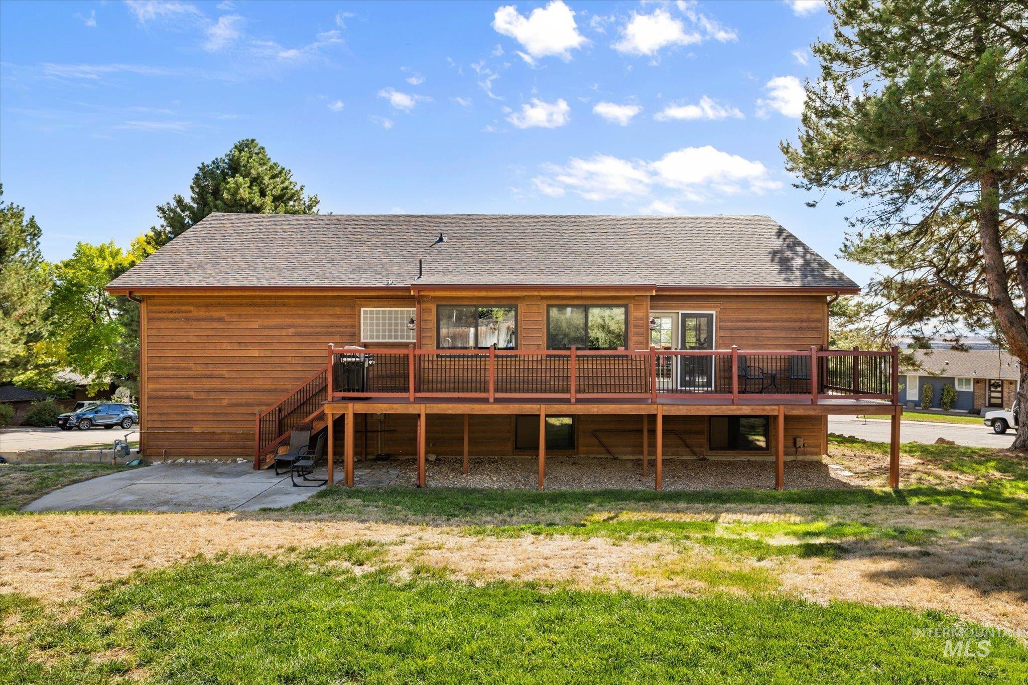Back of property featuring a deck, roof with shingles, stairs, and a lawn