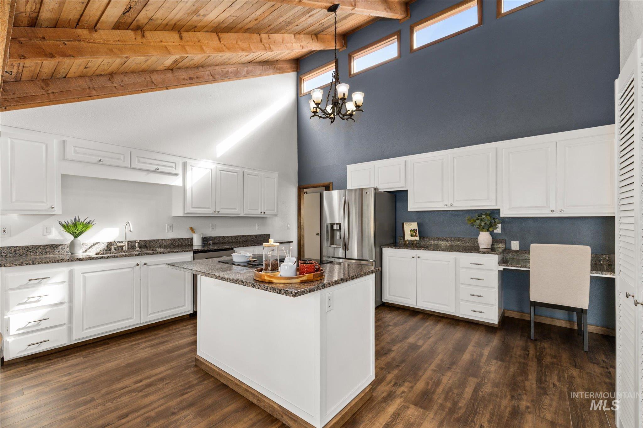 Kitchen with high vaulted ceiling, dark stone countertops, white cabinetry, decorative light fixtures, and dark wood-style flooring