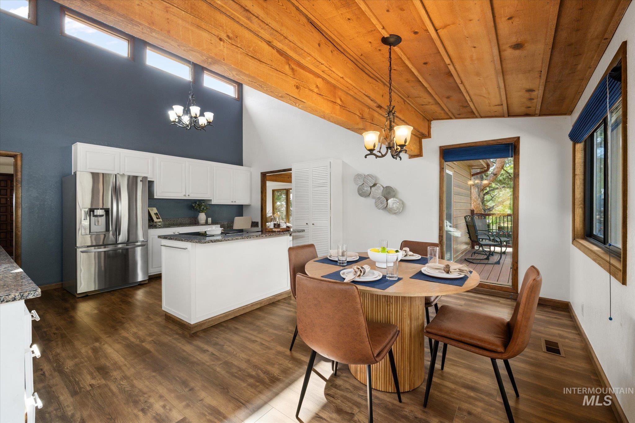 Dining space with healthy amount of natural light, a chandelier, dark wood-style floors, a towering ceiling, and wooden ceiling