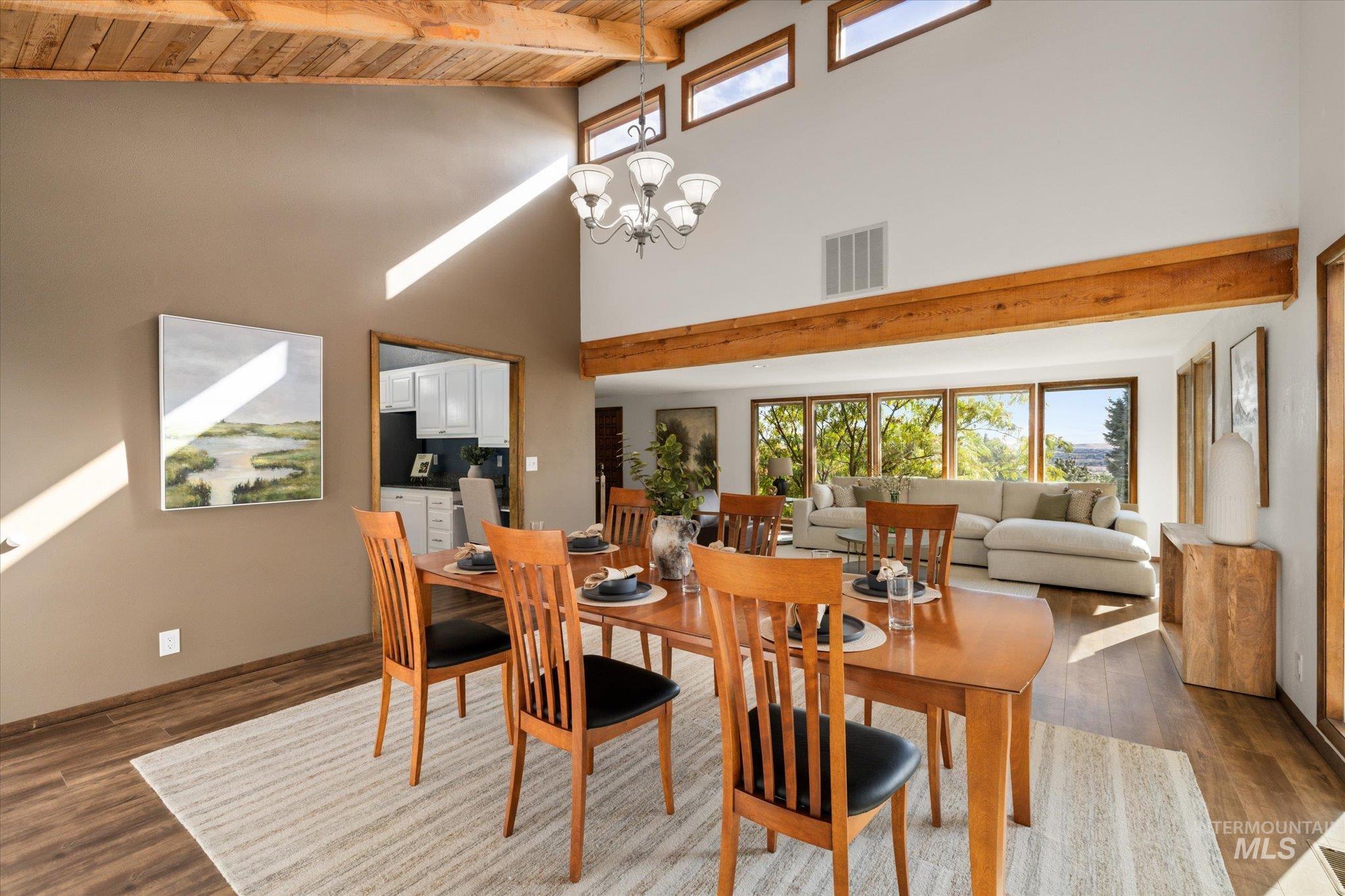Dining room featuring healthy amount of natural light, a towering ceiling, dark wood finished floors, a wood ceiling with exposed beams, and a chandelier