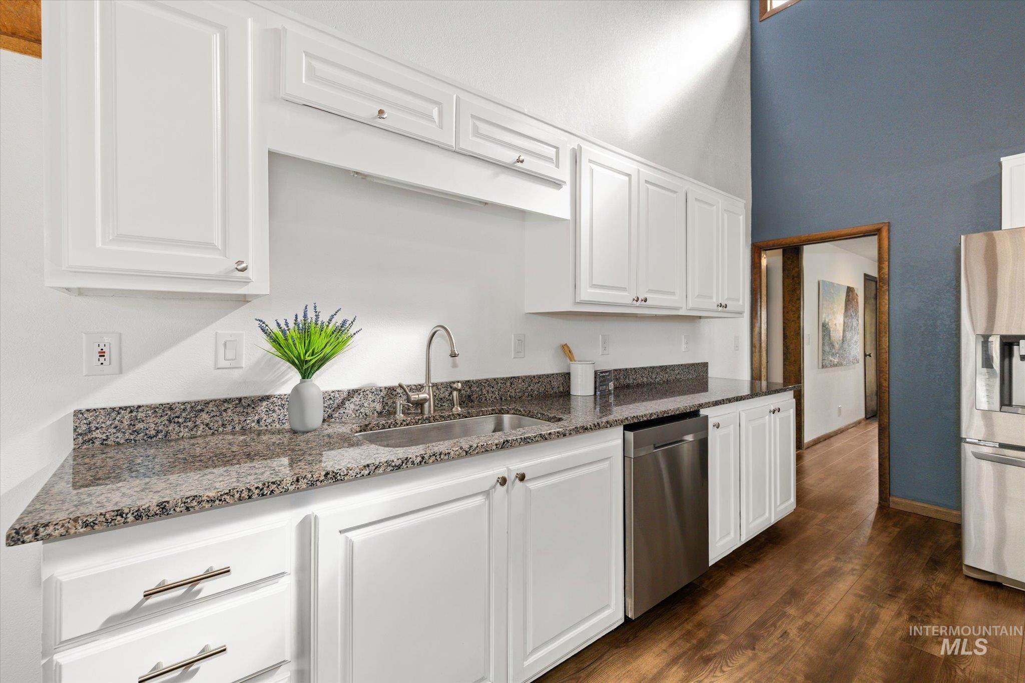 Kitchen with white cabinetry, dark stone countertops, dark wood-style flooring, stainless steel appliances, and a towering ceiling