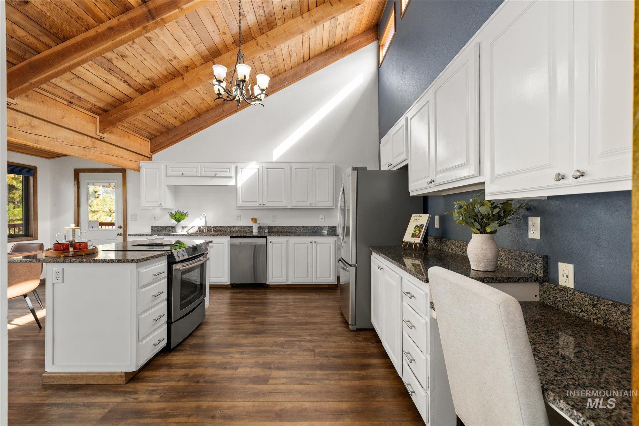 Kitchen with white cabinetry, pendant lighting, appliances with stainless steel finishes, dark wood-style floors, and dark stone countertops
