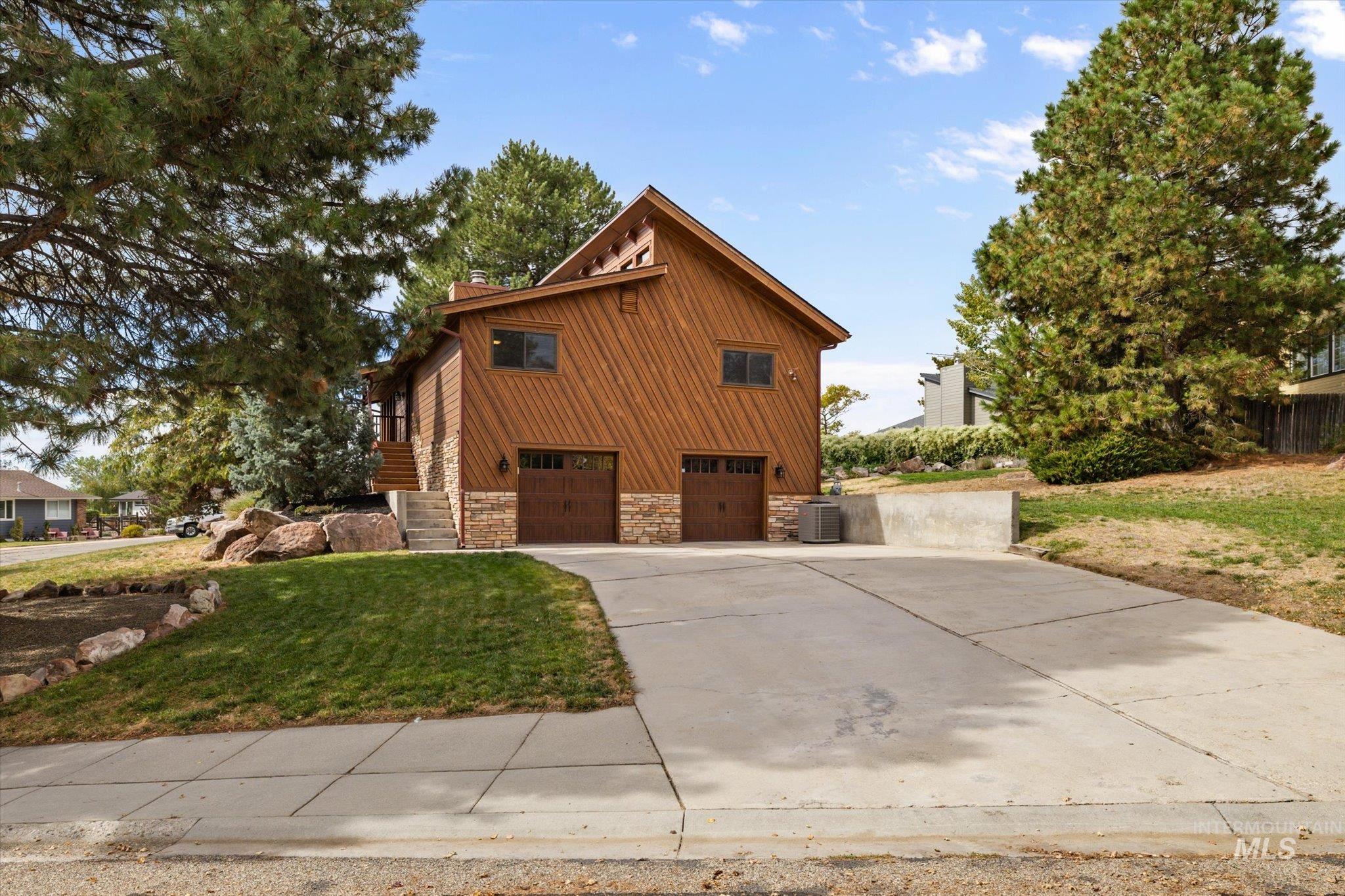 View of side of home featuring stone siding, driveway, a lawn, a chimney, and a garage