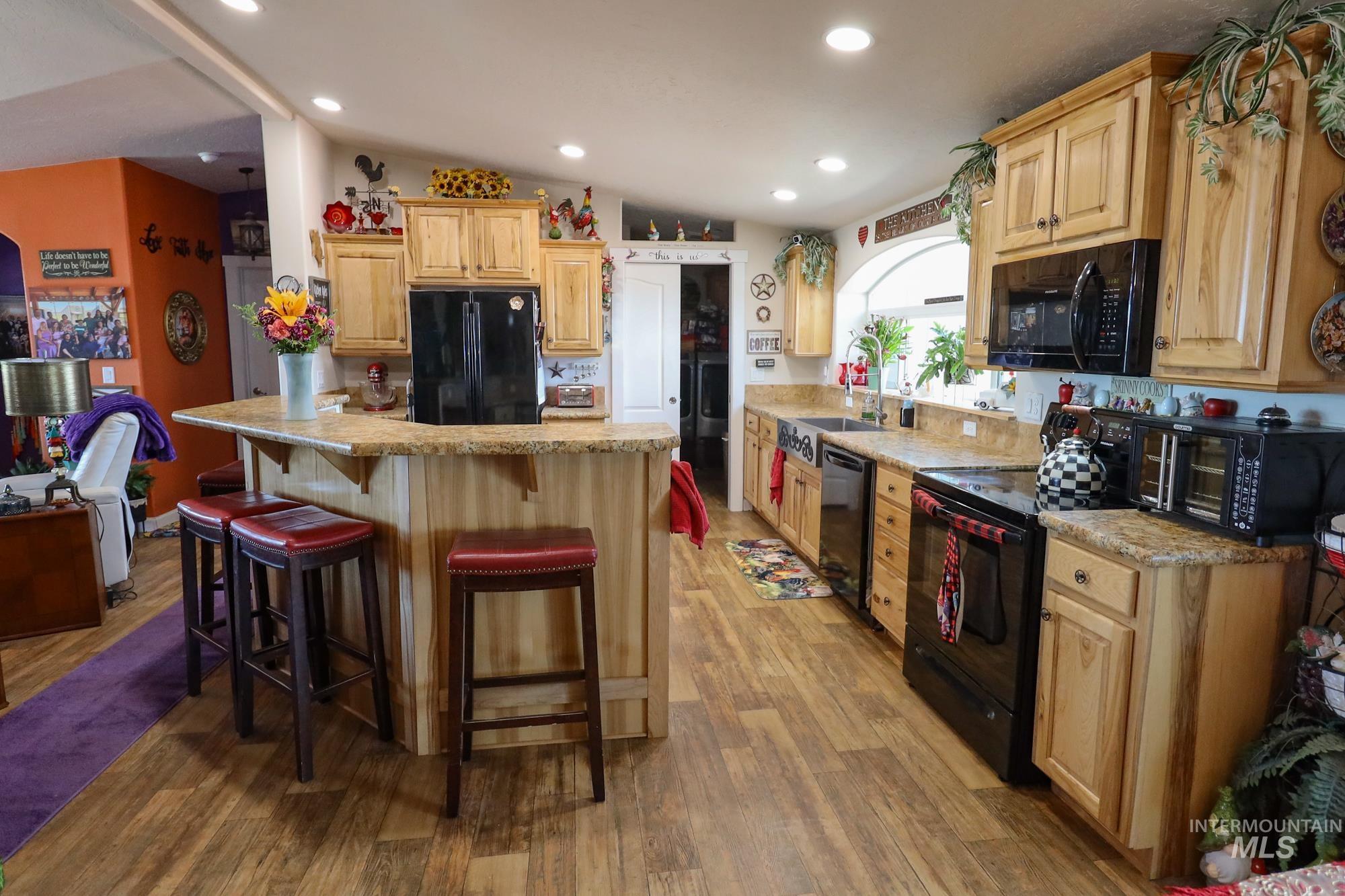 Kitchen with black appliances, a kitchen bar, light brown cabinetry, light wood-style flooring, and recessed lighting