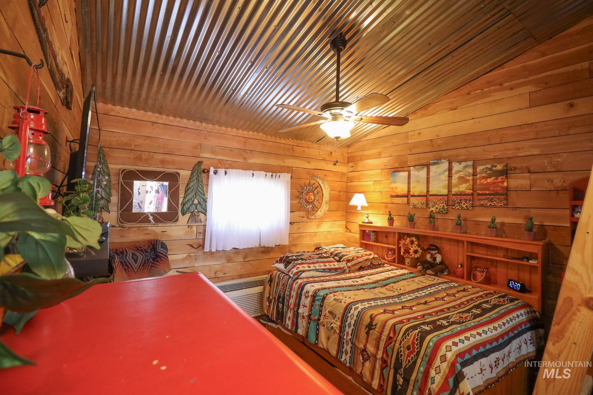Bedroom featuring wood walls, vaulted ceiling, and ceiling fan