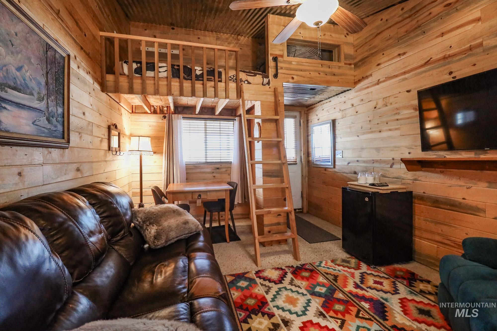 Carpeted living area featuring wooden walls, wooden ceiling, and a ceiling fan